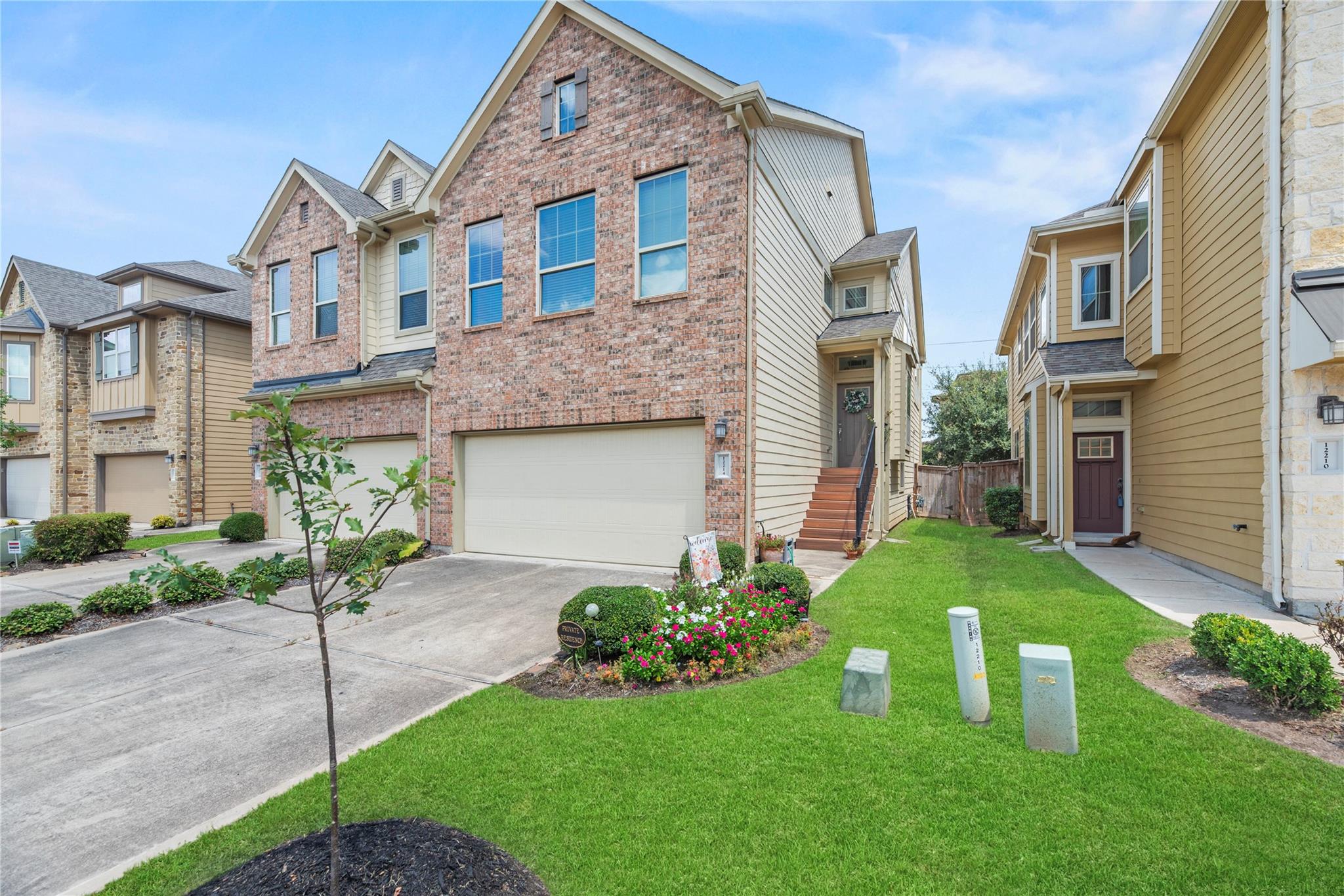 Brick townhome with a two-car garage, side-entry steps, and flower beds beside a green lawn.
