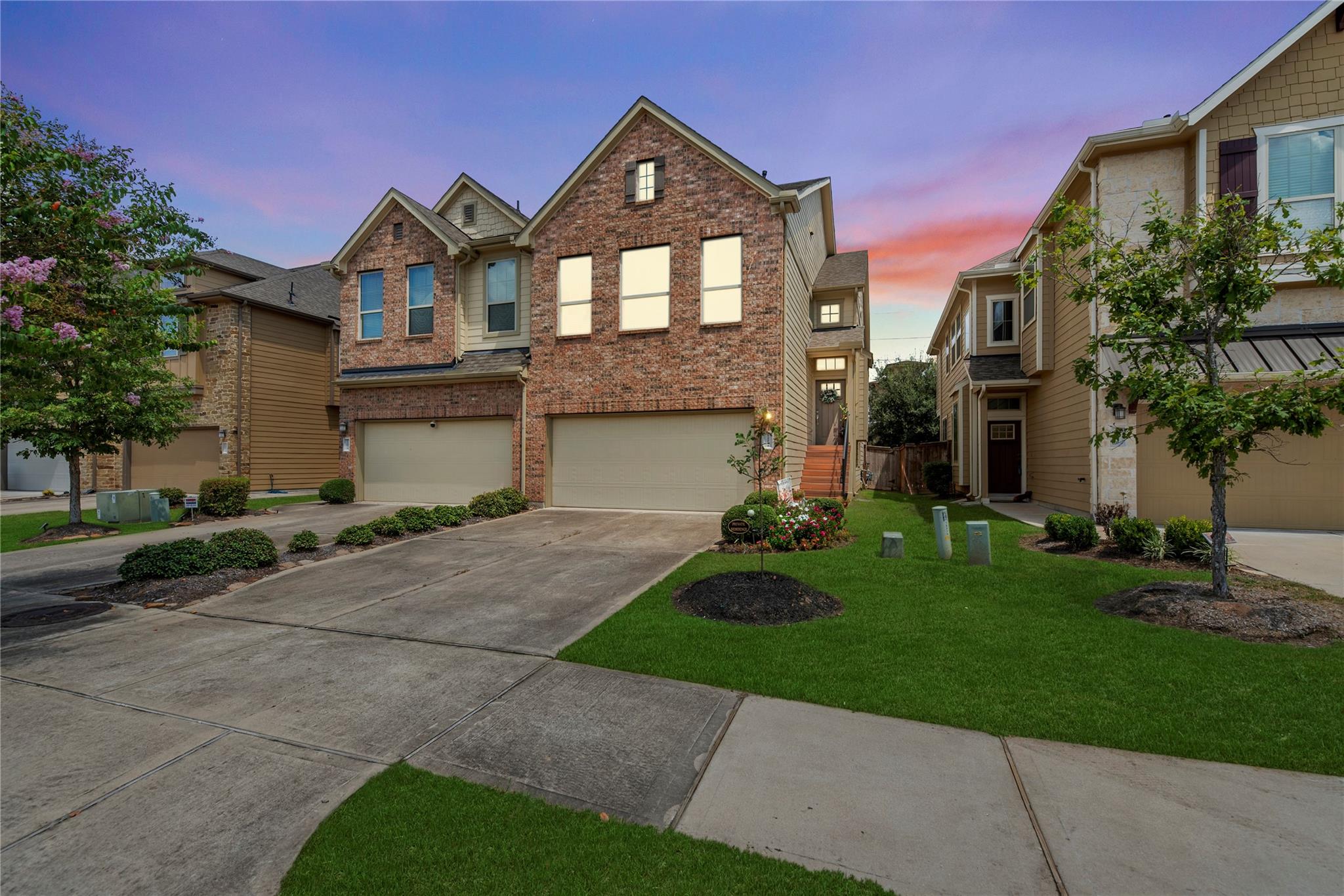 Two-story brick home with attached garages and landscaped lawn at dusk.