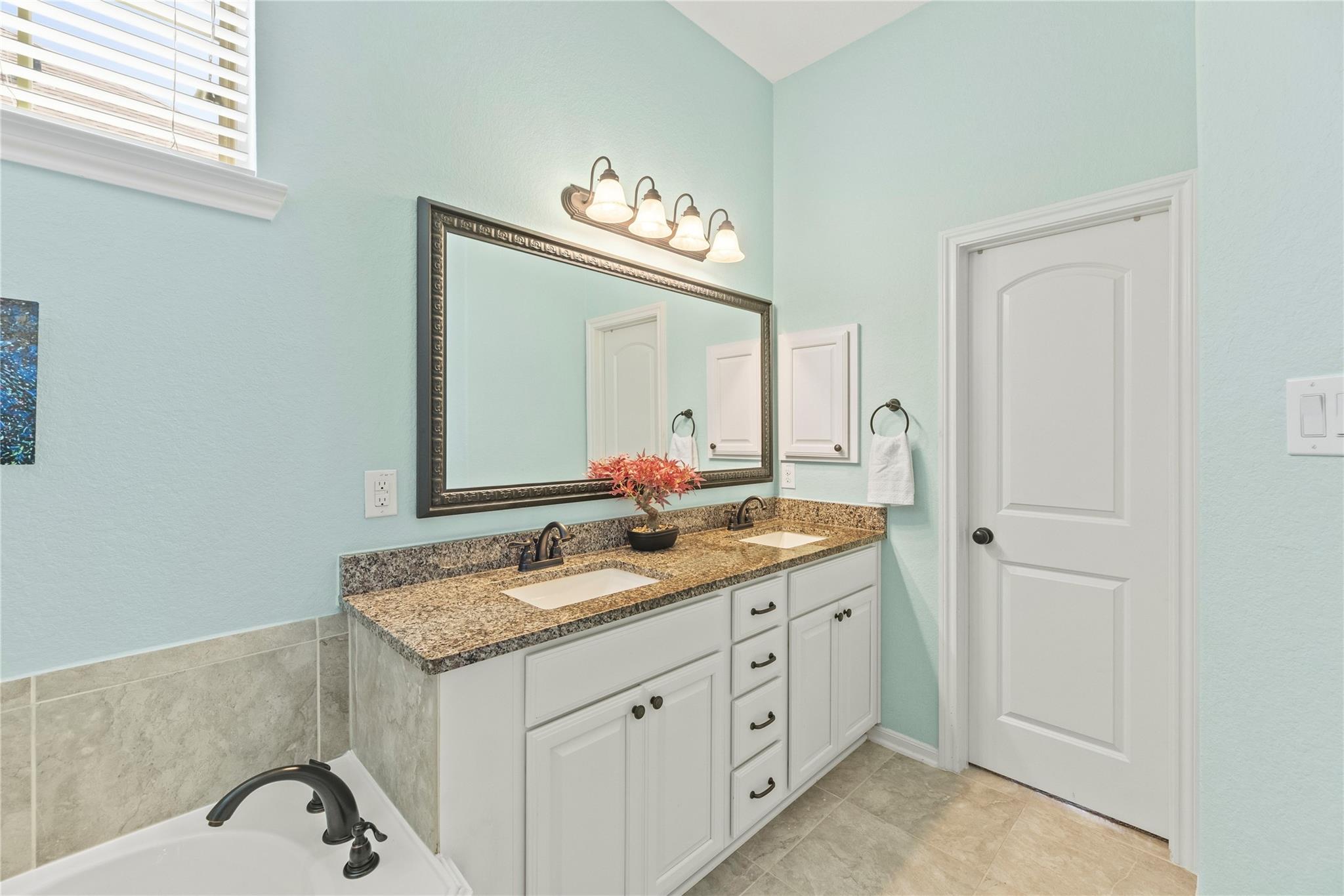 Bathroom with a double-sink white vanity, granite countertop, and large framed mirror.