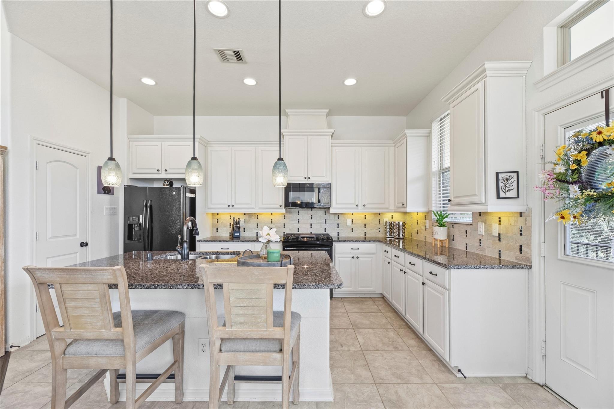 Kitchen with white cabinetry, granite counters, tiled backsplash, and a breakfast island with two chairs.