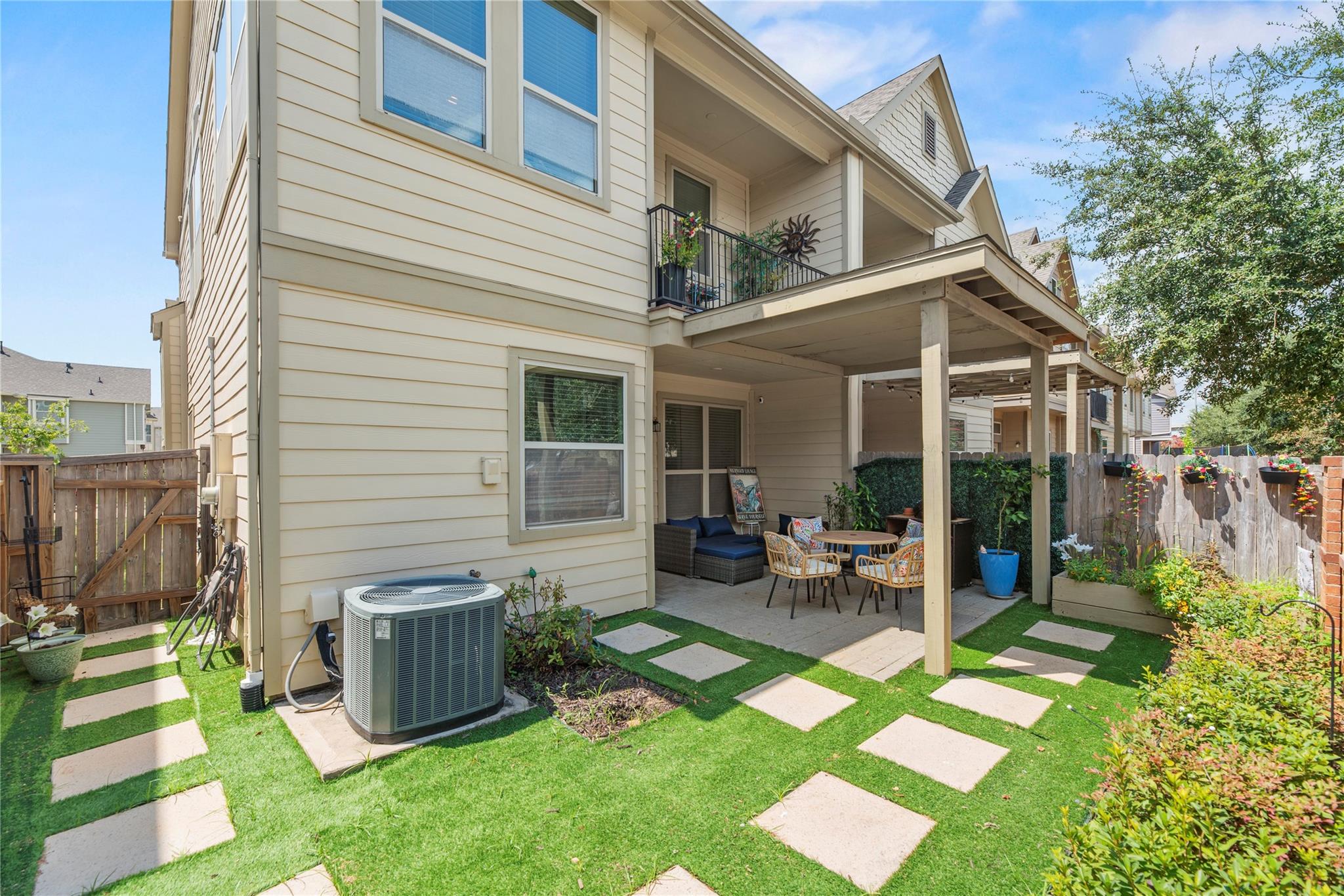 Home’s rear patio with outdoor seating beneath a covered deck, upper balcony, and stepping-stone lawn.