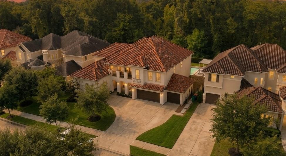 Aerial view of a beige, tile-roofed home with a broad driveway and landscaped yard.
