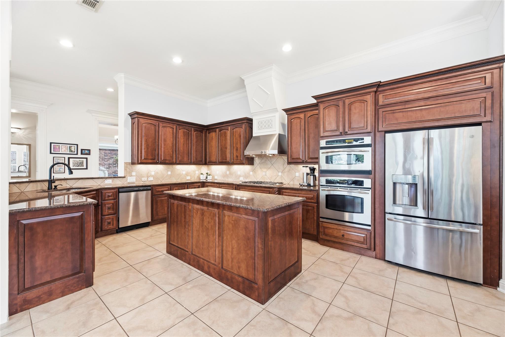 Kitchen with dark wood cabinets, a central island, and stainless steel double oven and refrigerator.