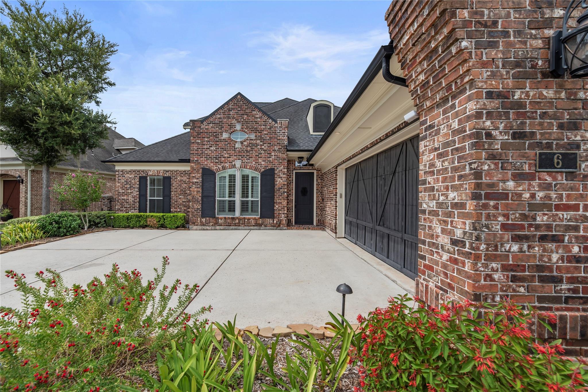 Brick home with a carriage-style garage door, wide driveway, and flowering landscaping.