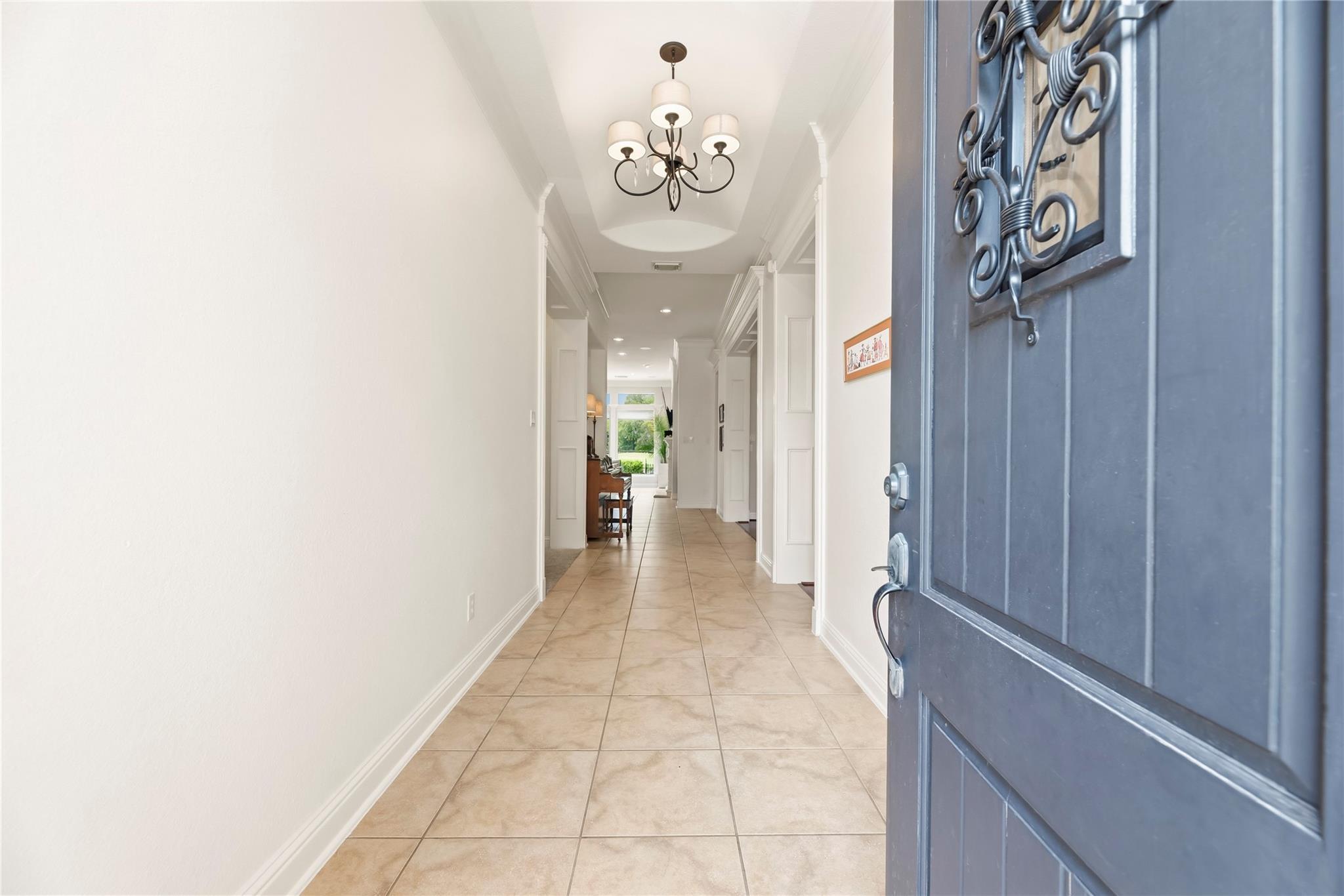 Entry hallway with beige tile floors, a dark chandelier, and an open blue front door.