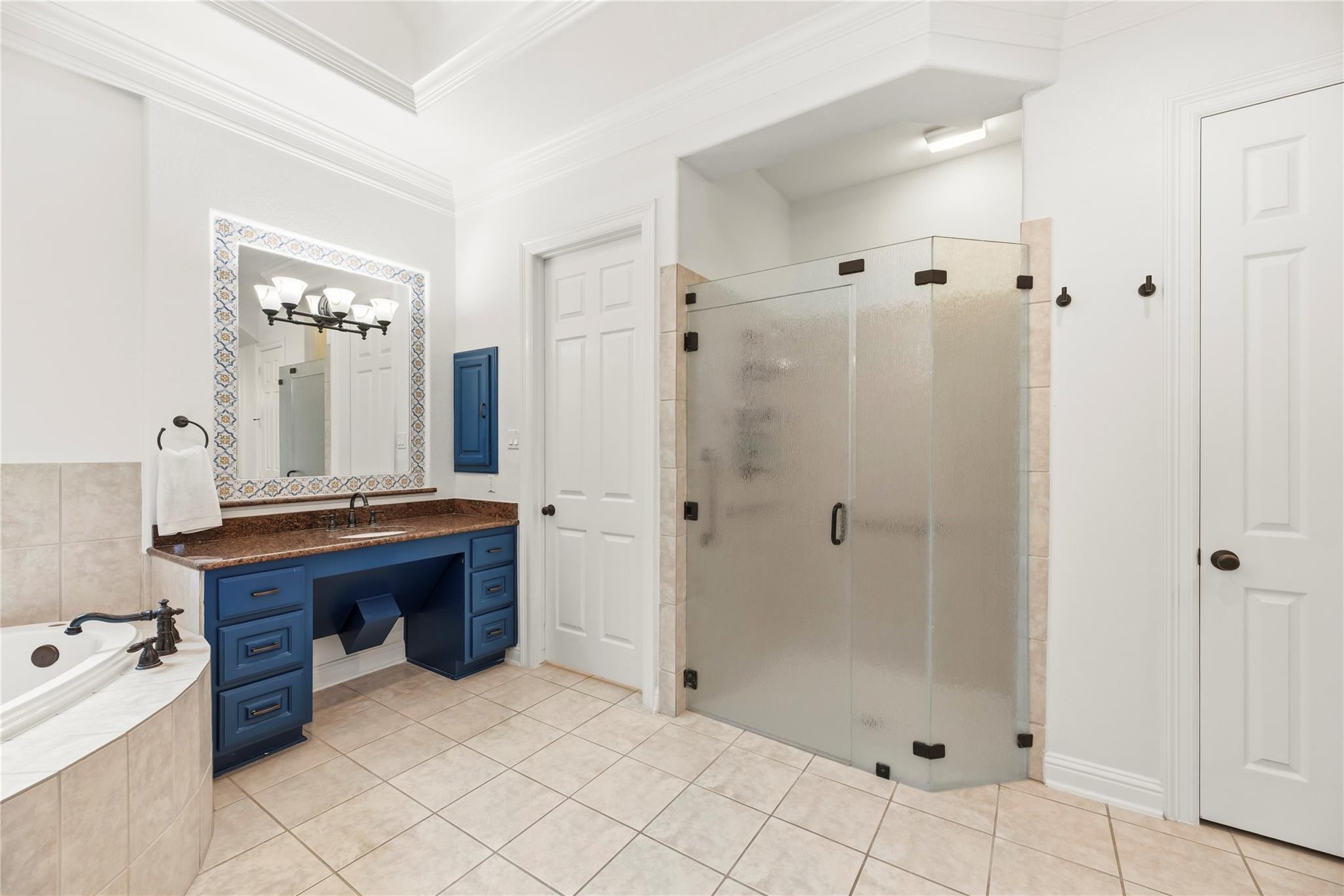 Bathroom with a blue vanity, patterned mirror frame, glass shower, and corner soaking tub.