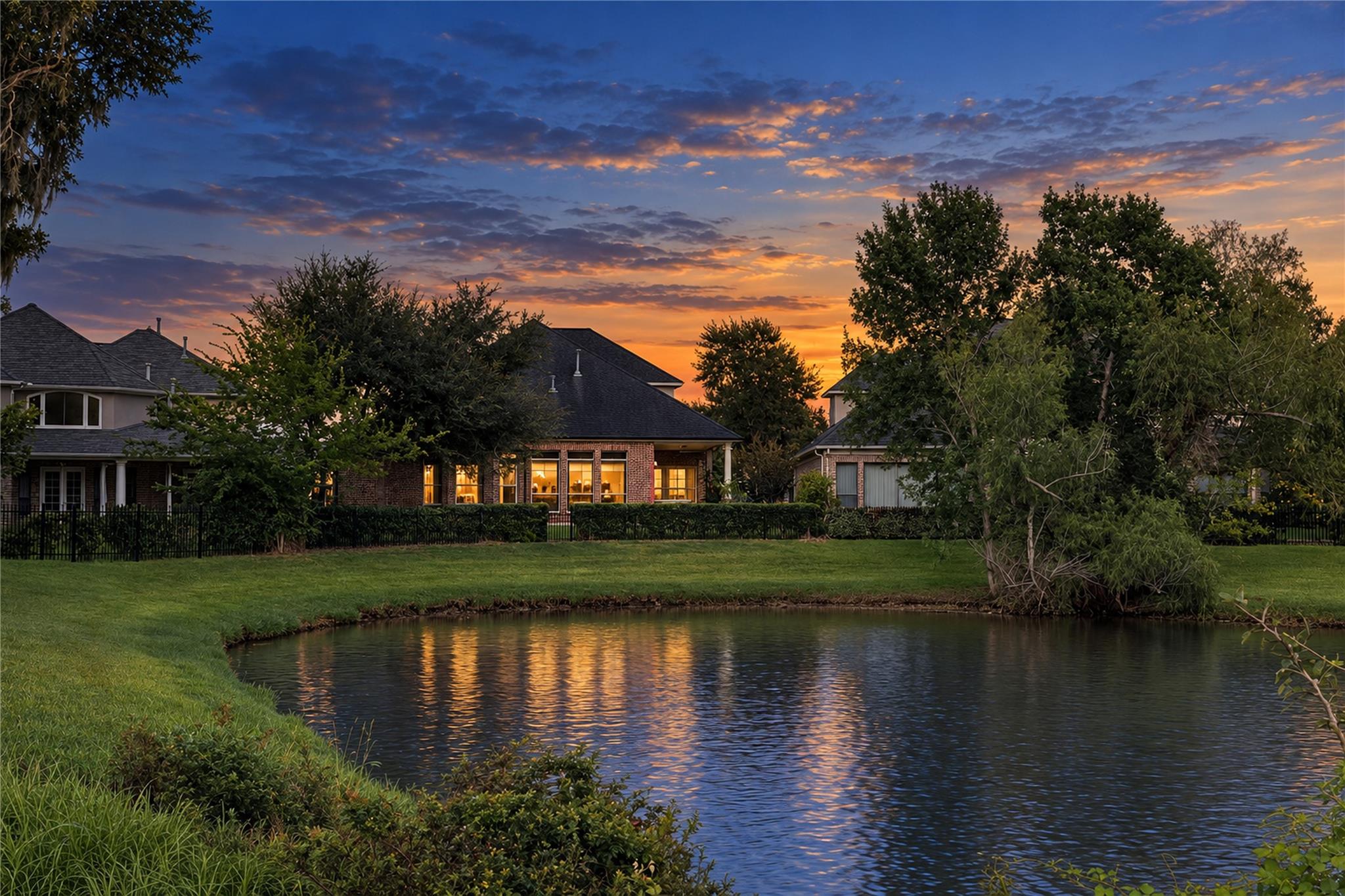 Brick home glowing at dusk across a pond reflecting the sunset sky.