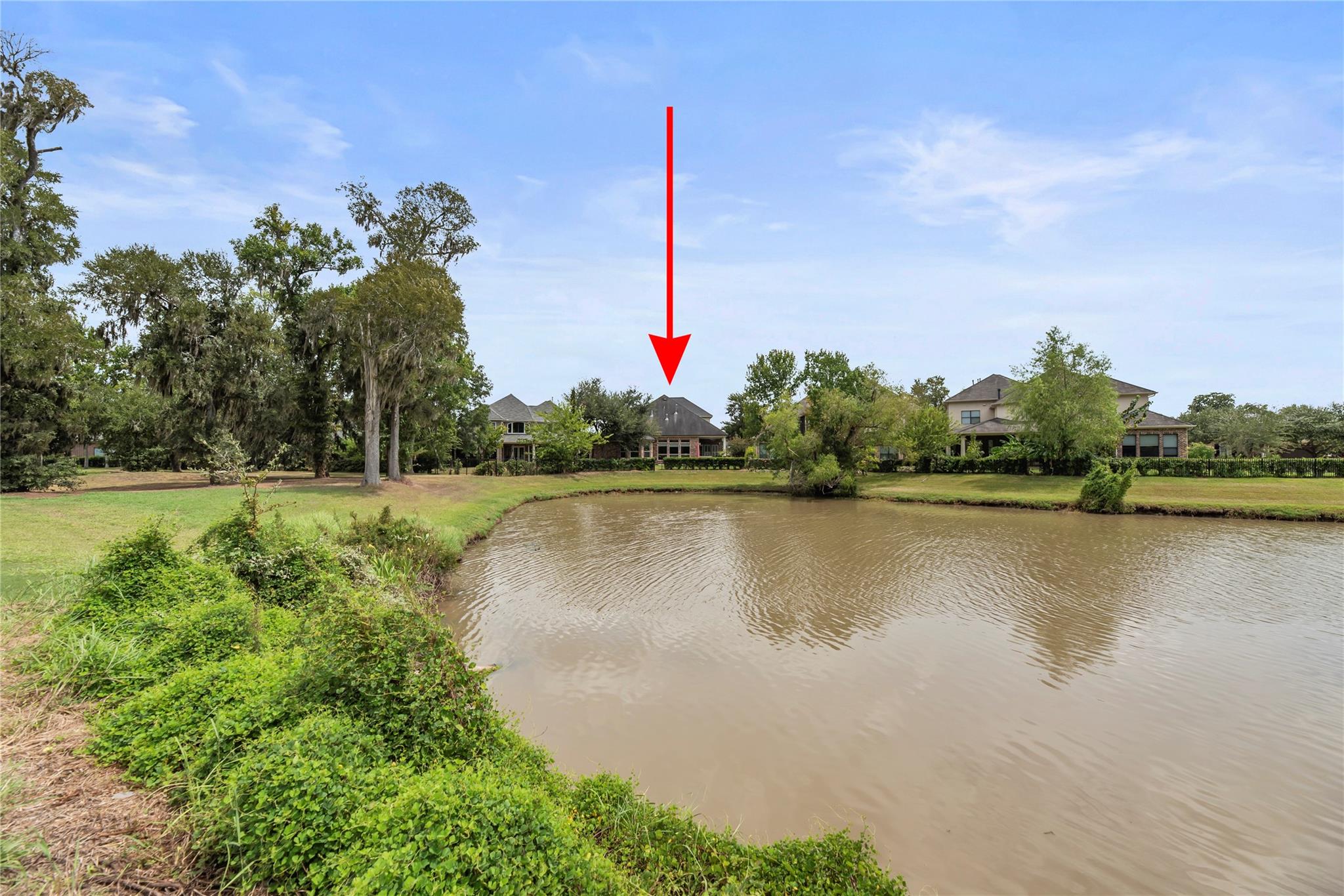 Home across a pond, marked by a red arrow, with mature trees along the shoreline.
