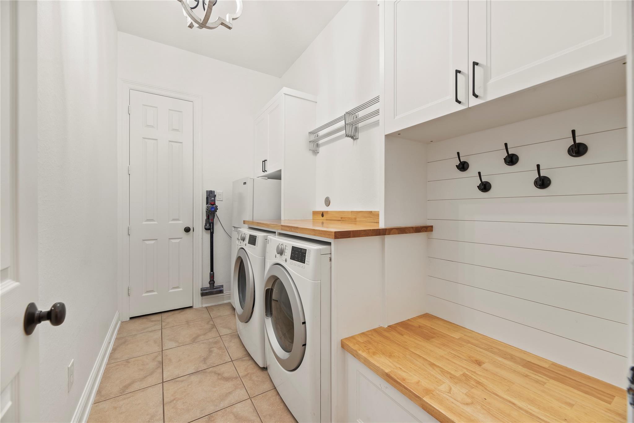 Laundry room with front-loading washer and dryer, butcher-block counters, and black wall hooks.