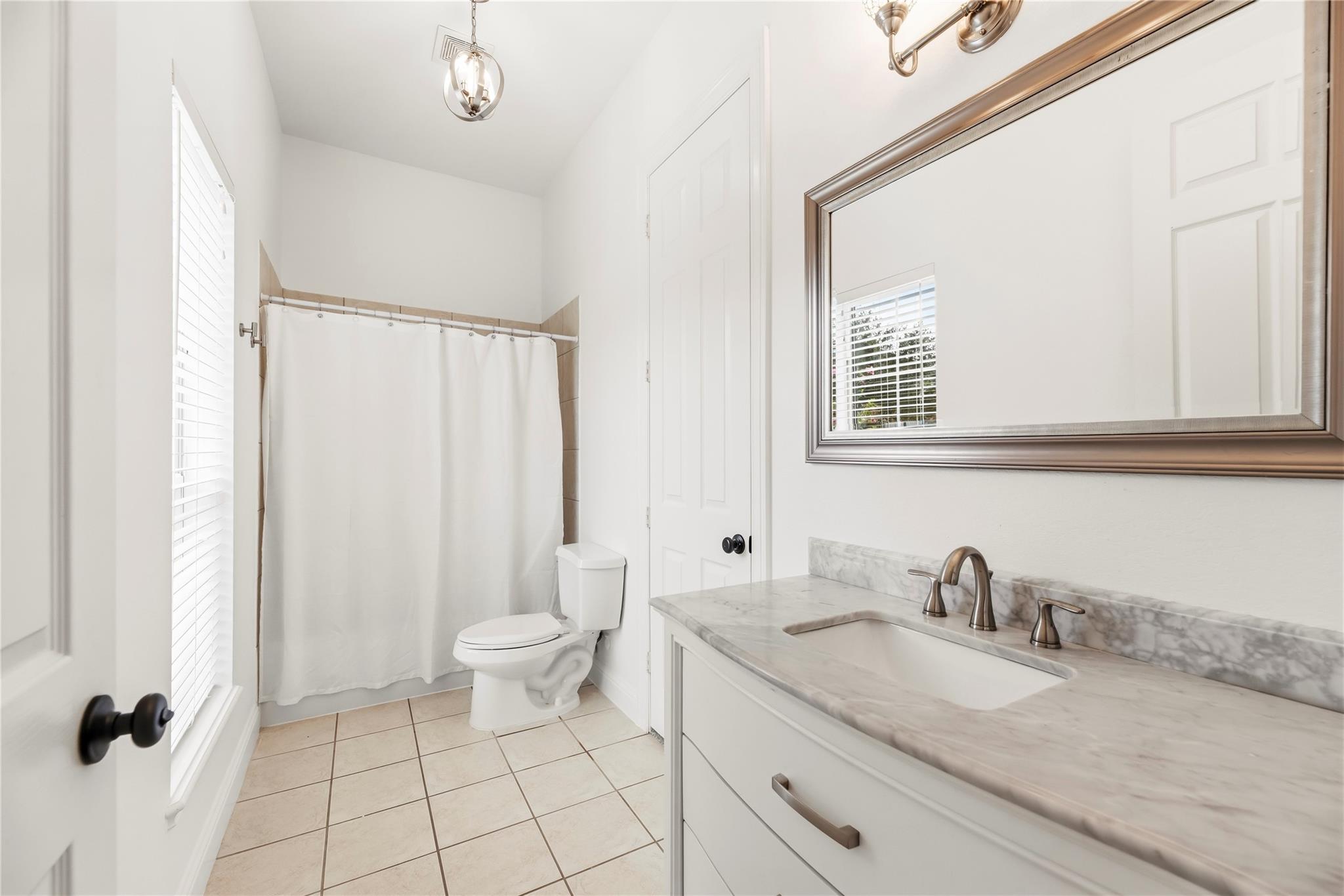 Bathroom with a marble-look vanity, large framed mirror, and curtained tub and shower.