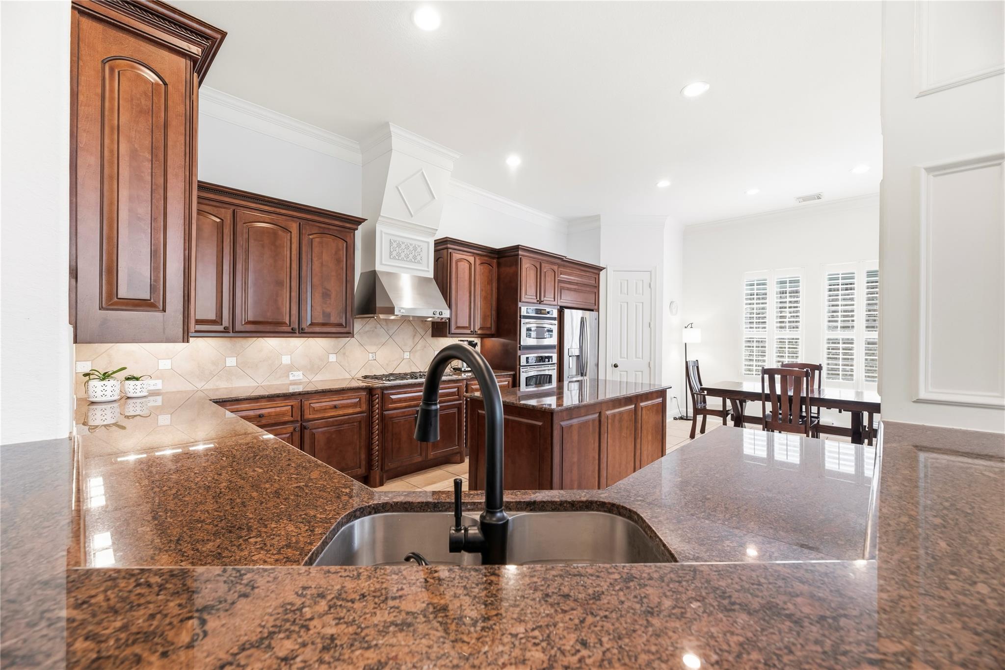 Kitchen with dark wood cabinets, granite counters, a large island, and stainless steel appliances.