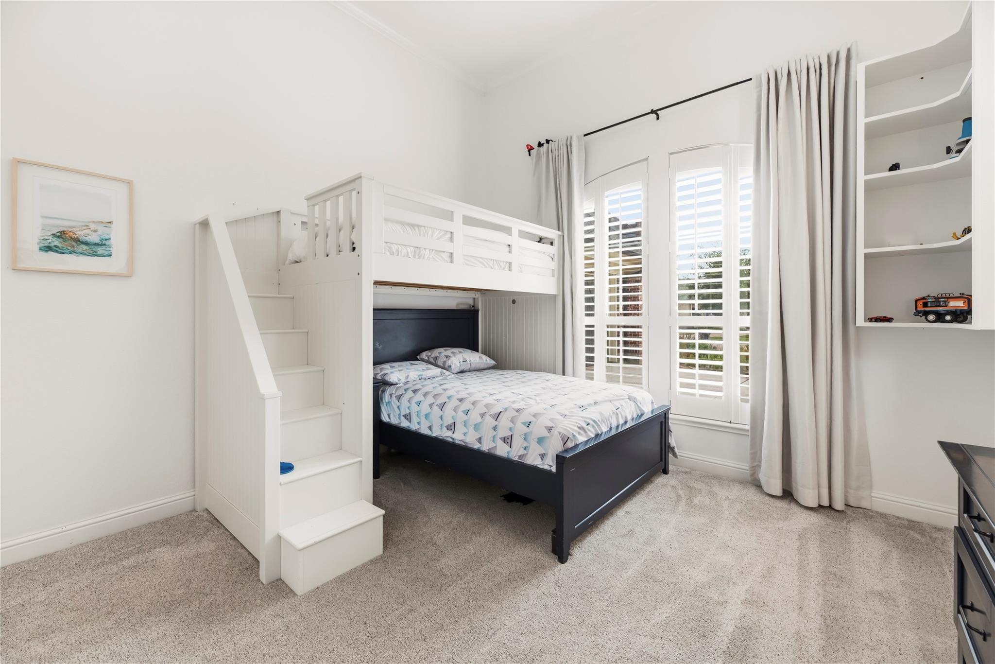 Bedroom with a white loft bunk over a dark-framed bed and plantation-shuttered windows.