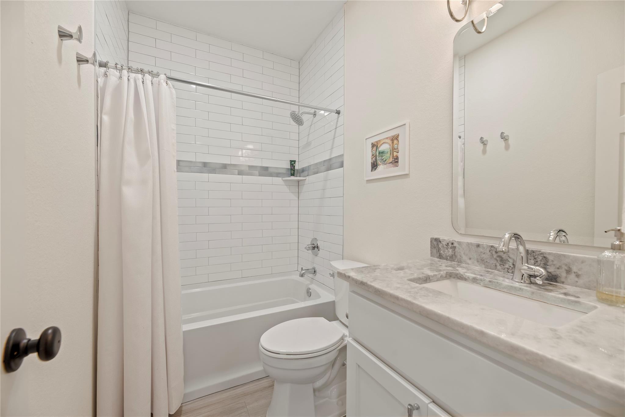 Bathroom with white subway-tile tub and shower, gray accent band, and marble-look vanity countertop.