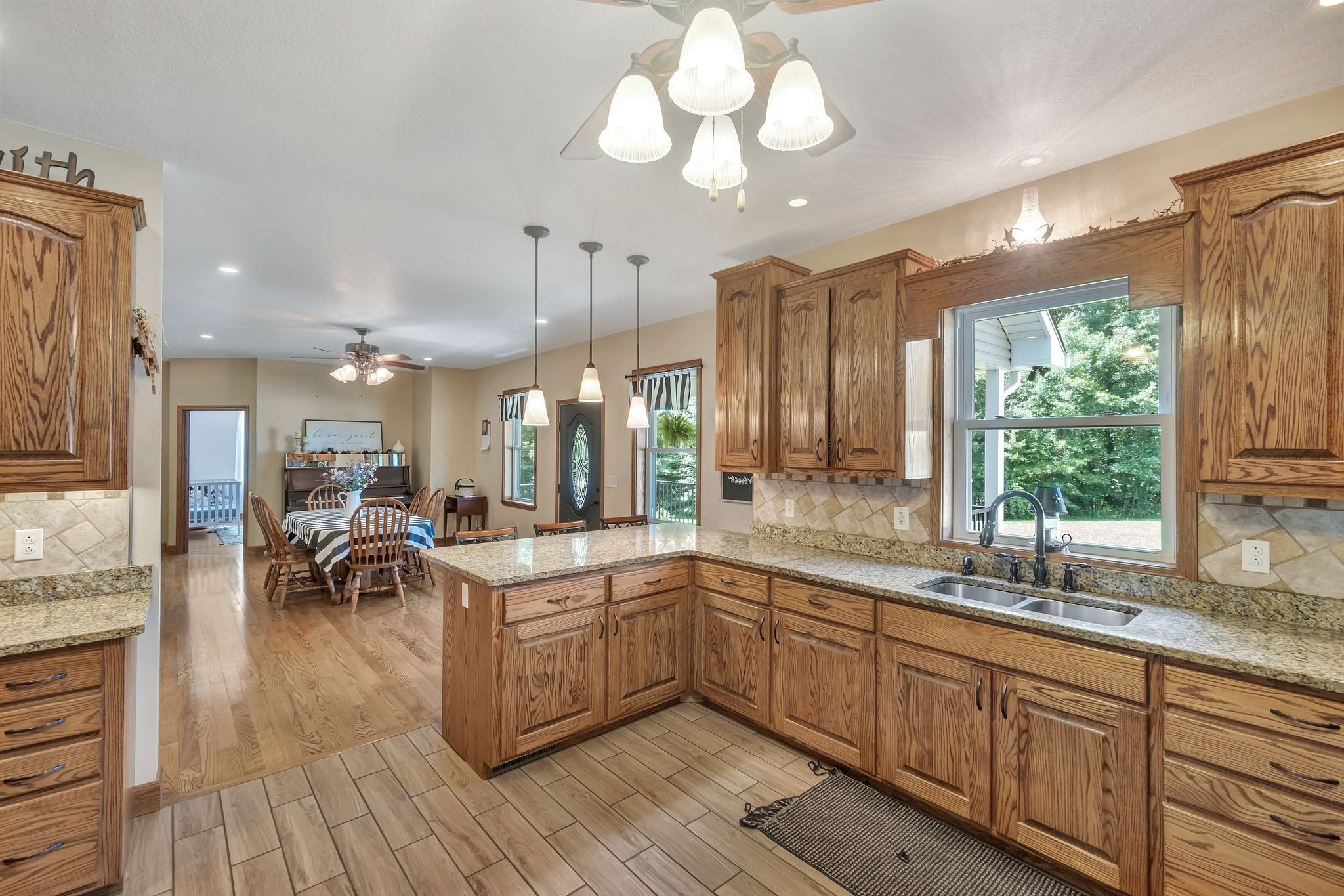 Oak kitchen with granite island and window-side sink, opening to a dining area.