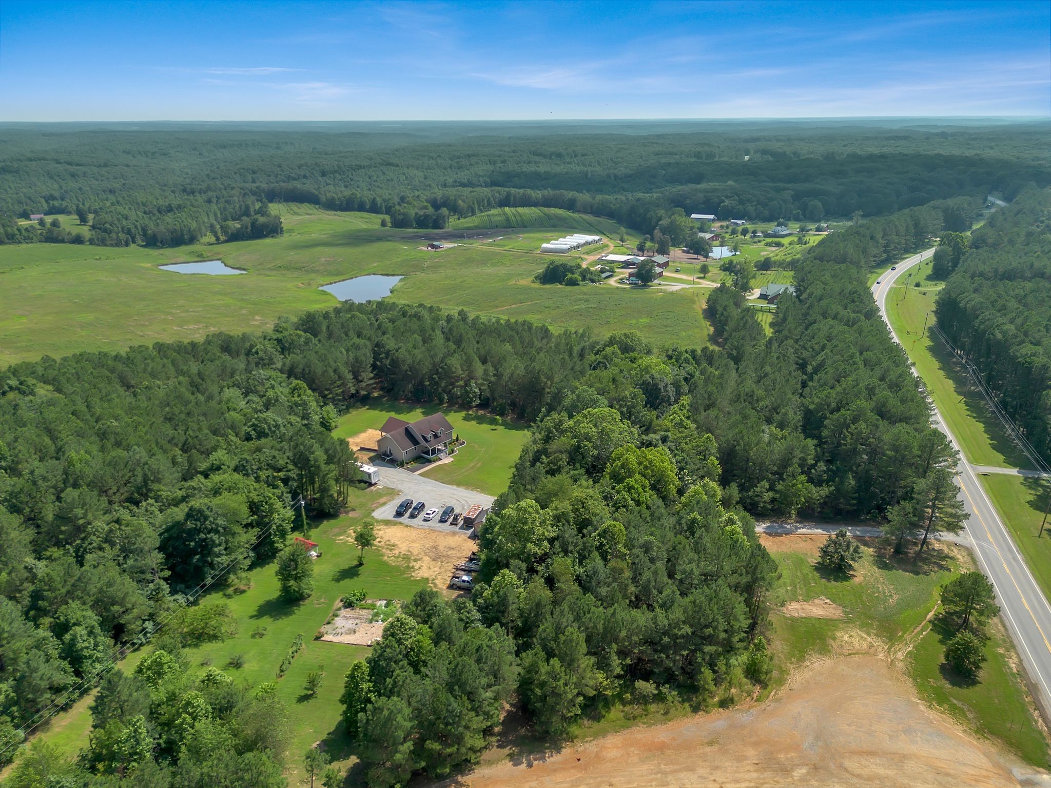 Aerial view of a rural home surrounded by woods, with open fields, two ponds, and a highway nearby.