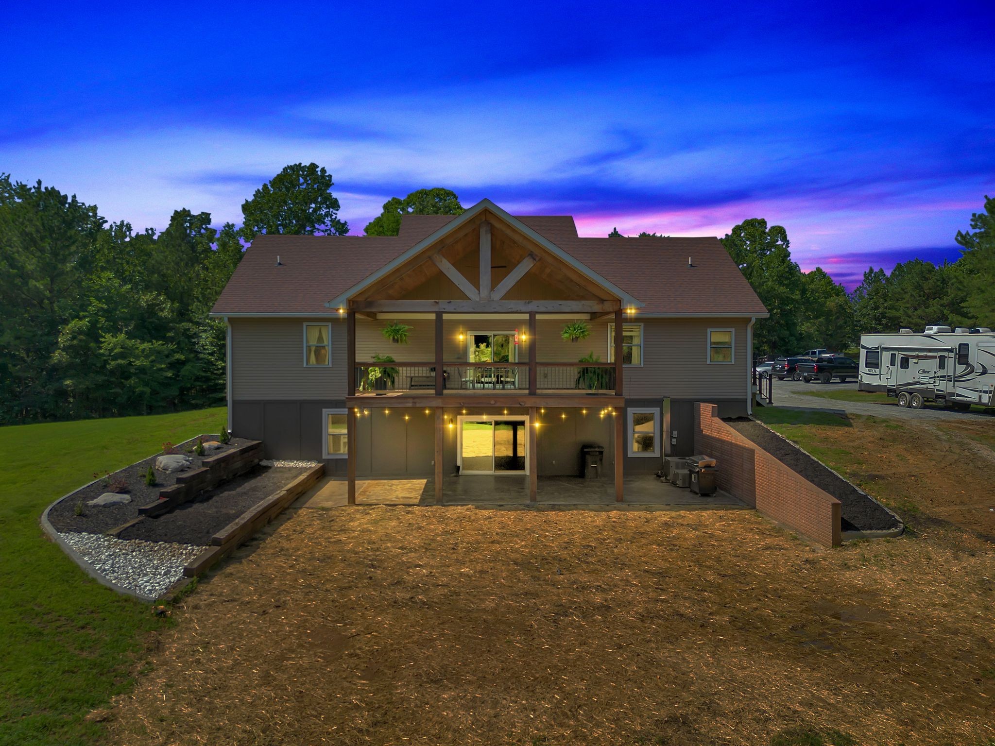 Two-story house at dusk with a timber-framed covered deck and illuminated lower patio.