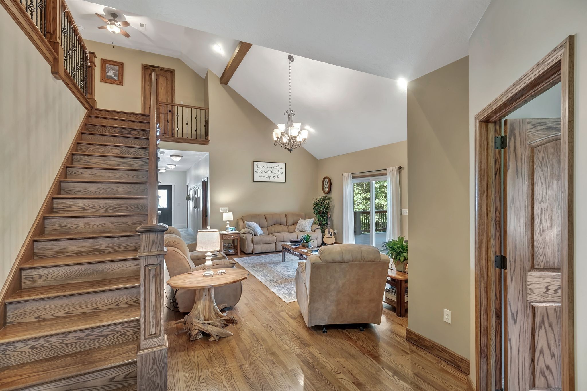 Living room with a vaulted ceiling, wood staircase, exposed beams, and sliding doors to a deck.