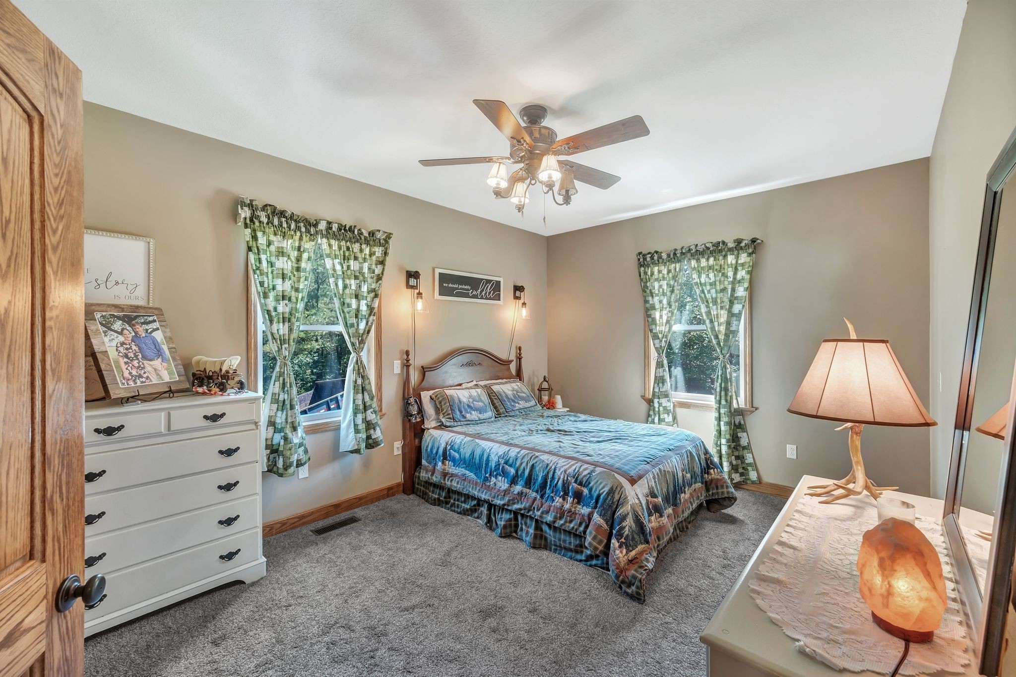 Furnished bedroom with blue patterned bedding, green curtains, and a ceiling fan.