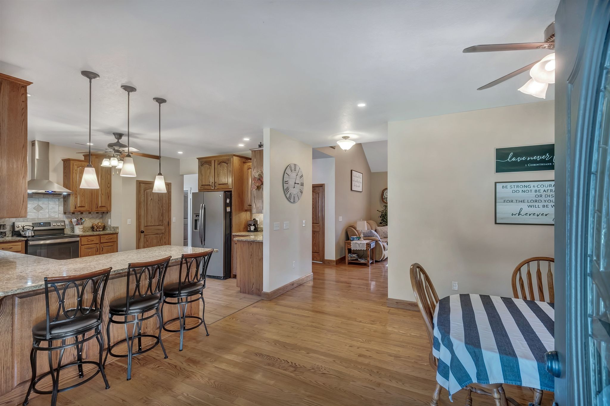 Open-plan kitchen and dining area with a granite island, wood cabinetry, stainless steel appliances, and striped tablecloth.