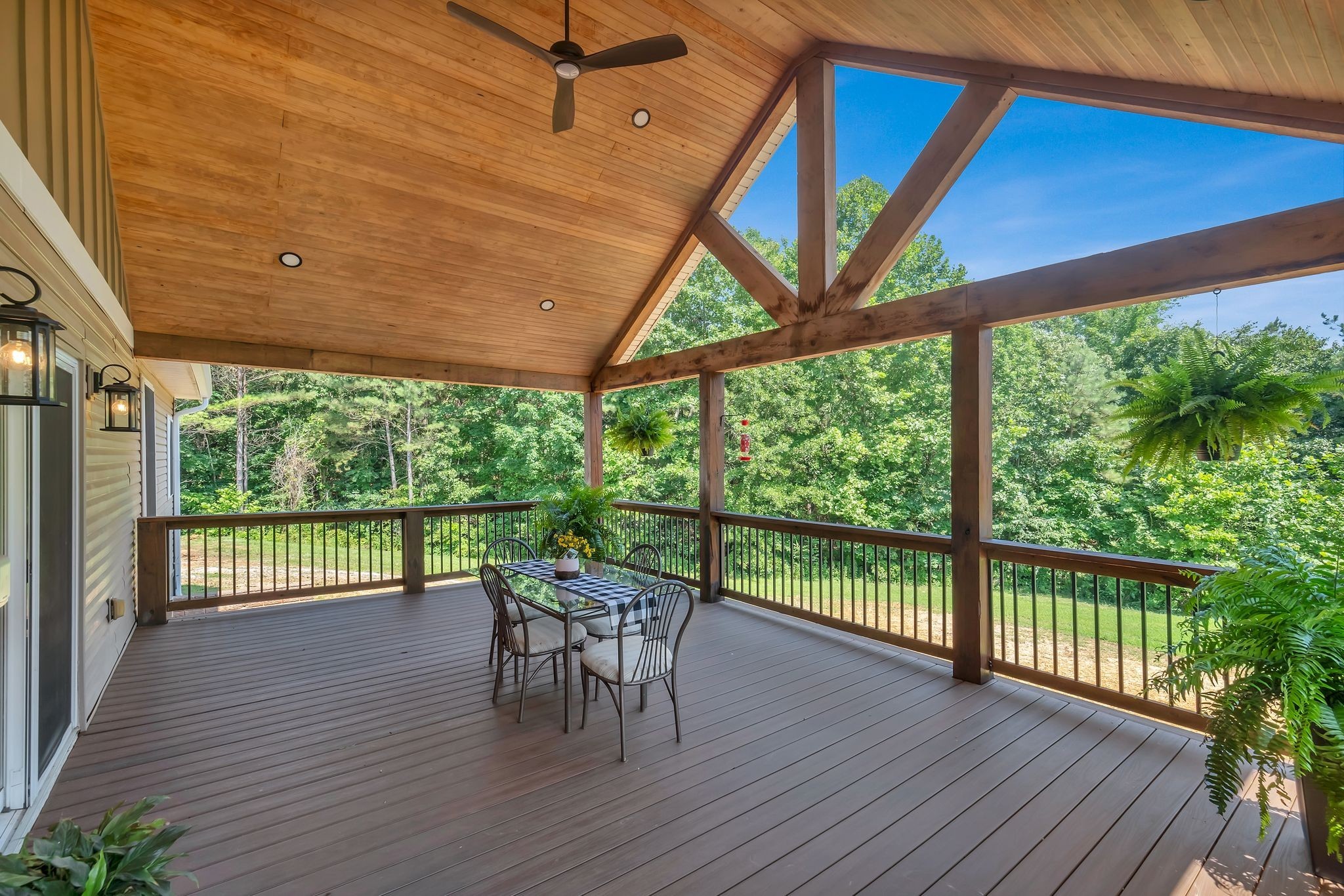 Covered deck with vaulted wood ceiling, timber beams, dining table, and wooded views.