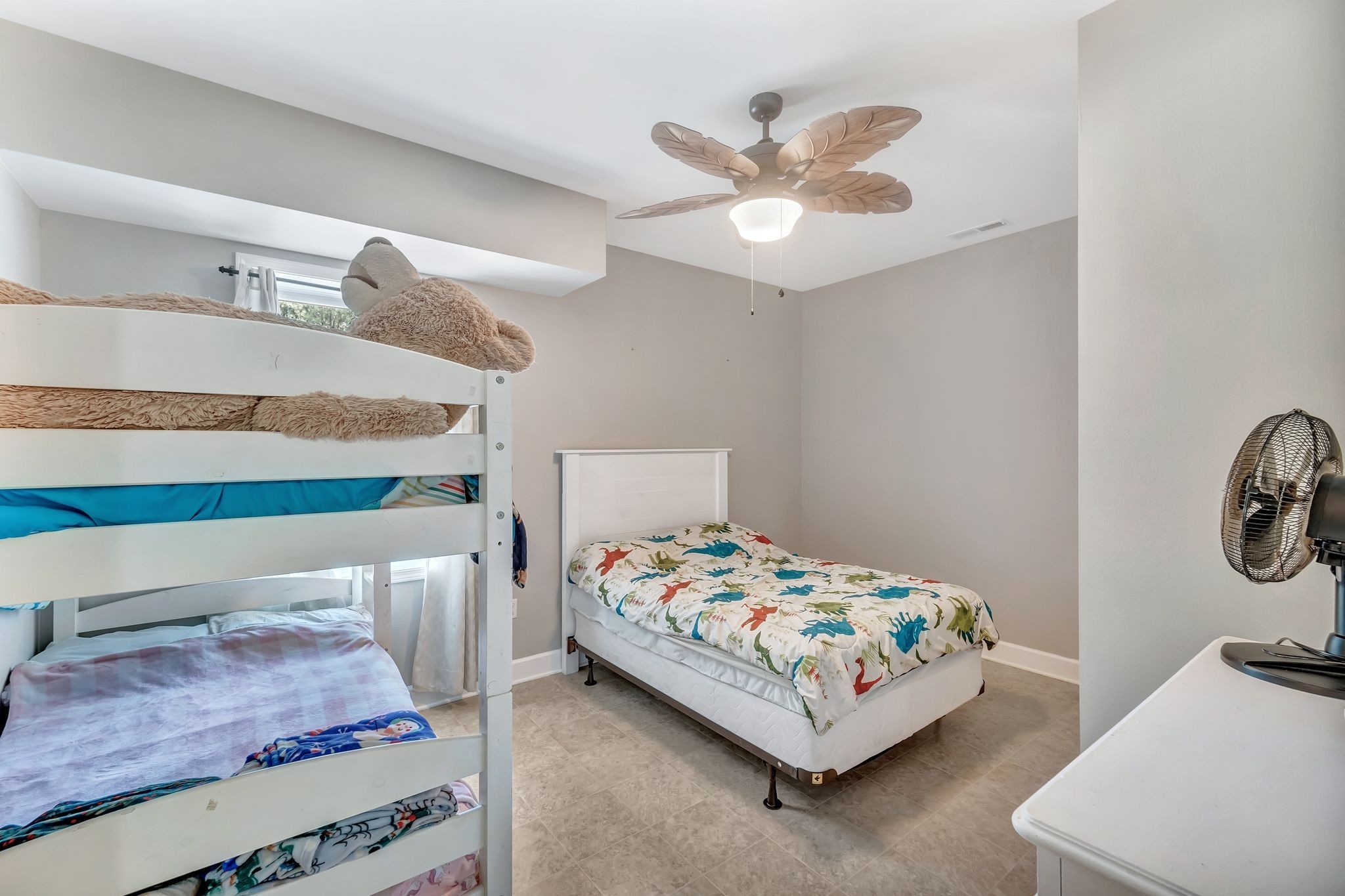 Bedroom with a white bunk bed, plush toys, and a separate bed with dinosaur-print bedding.