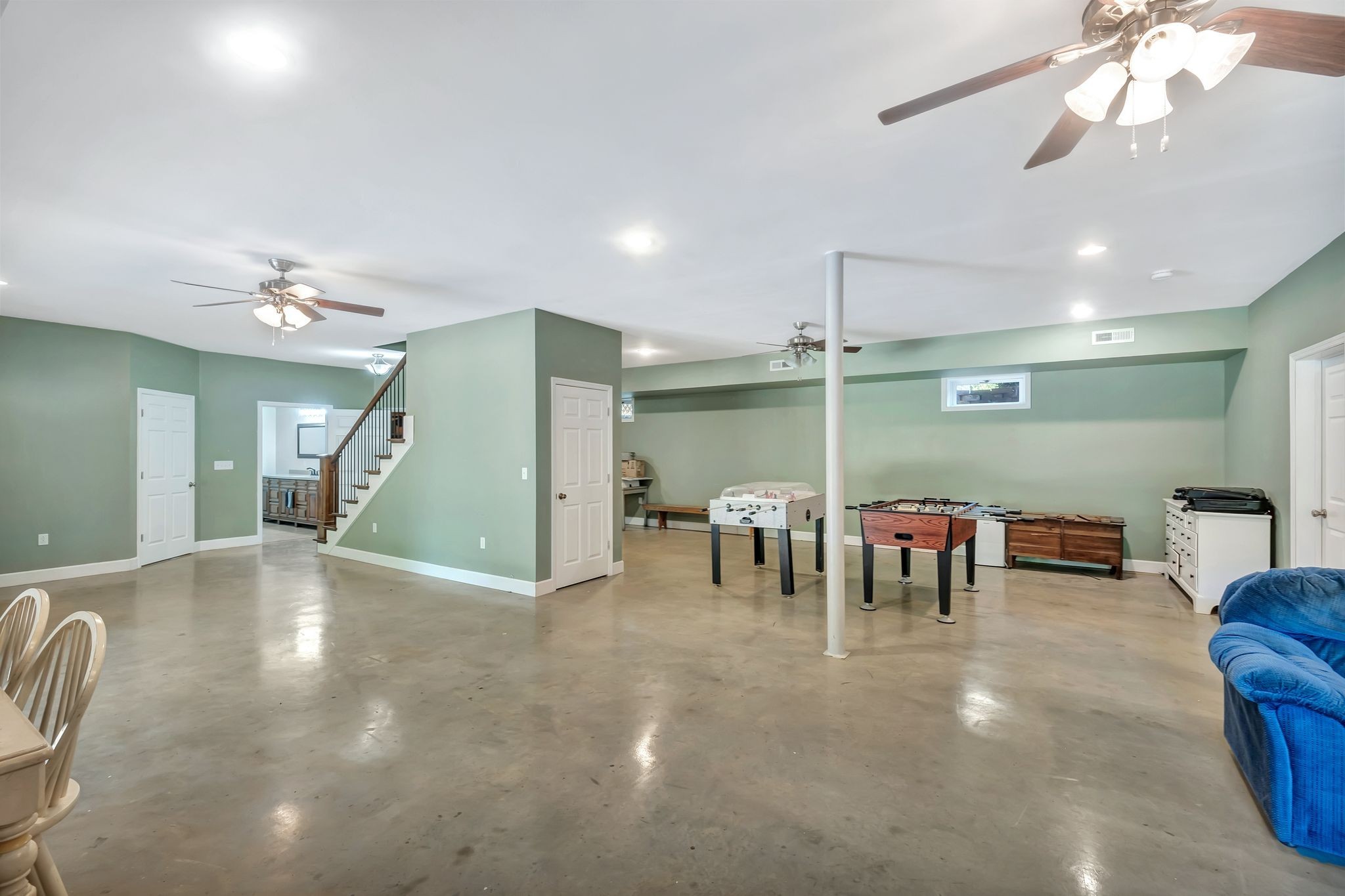 Spacious recreation room with sage-green walls, concrete floors, and foosball and air hockey tables.