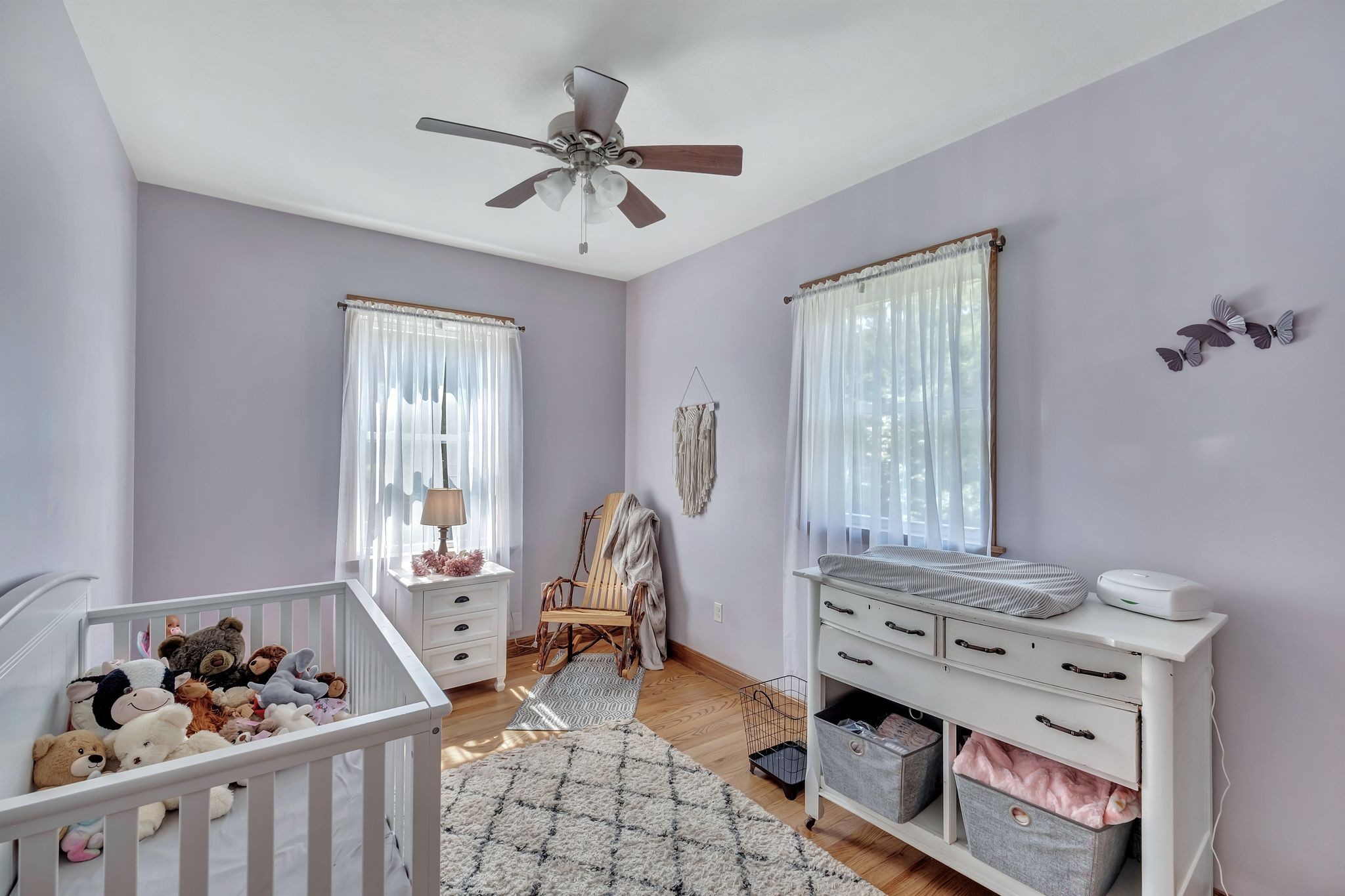Nursery with a toy-filled white crib, changing table, and wooden rocking chair.