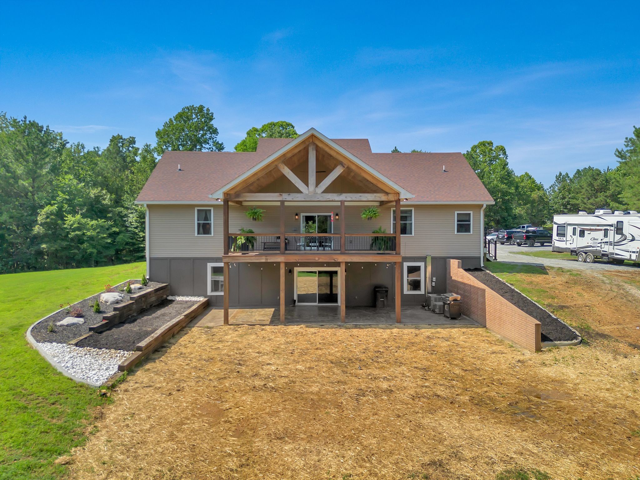 Rear of a two-story home with a covered timber porch, landscaped beds, and a broad yard.