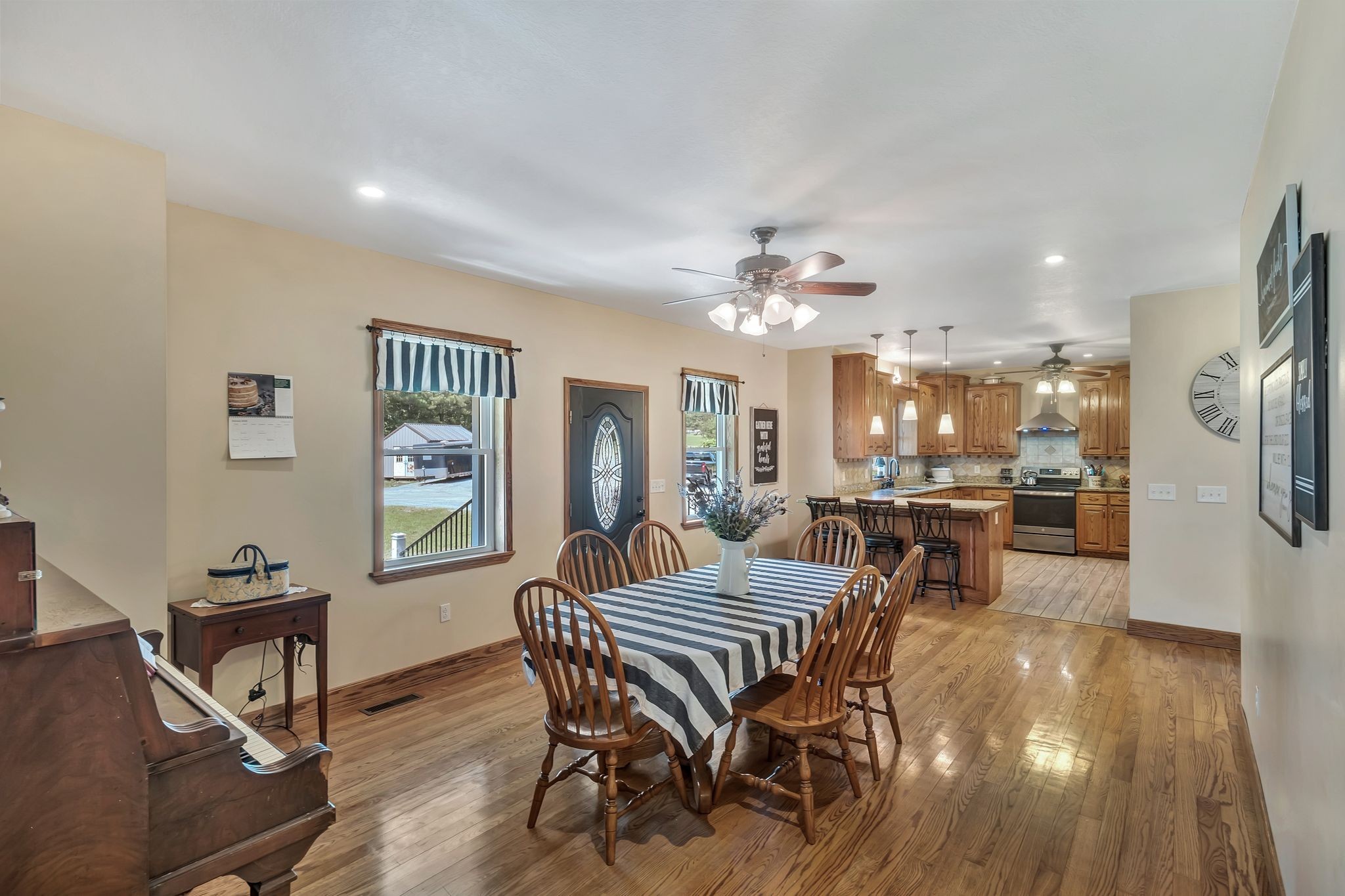 Dining room with a striped tablecloth, hardwood floors, and an open kitchen with wood cabinets.