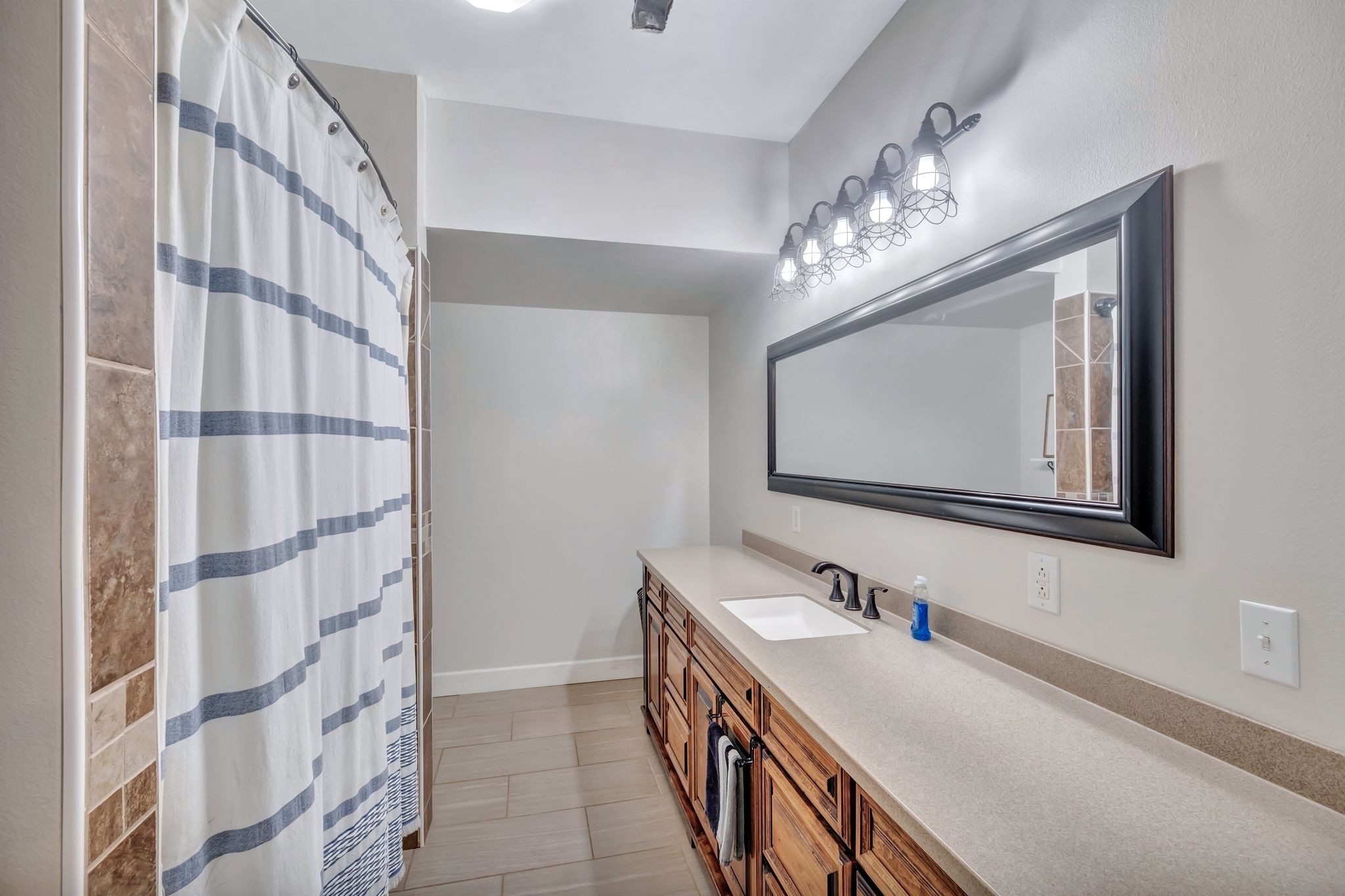 Bathroom with a long wood vanity, oversized framed mirror, and blue-striped shower curtain.