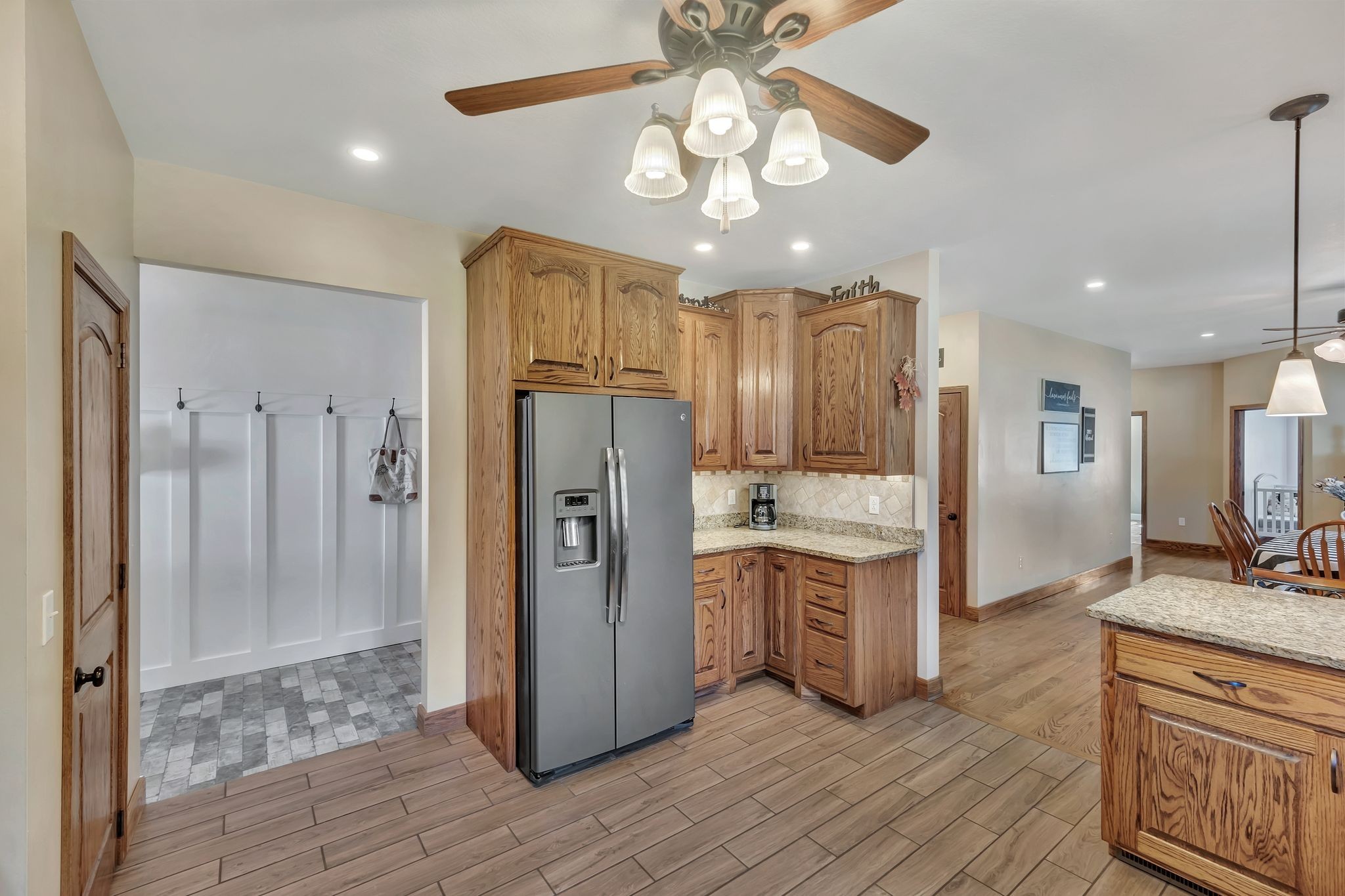 Kitchen with honey-toned wood cabinets, granite counters, and stainless-steel refrigerator beside a tiled laundry area.