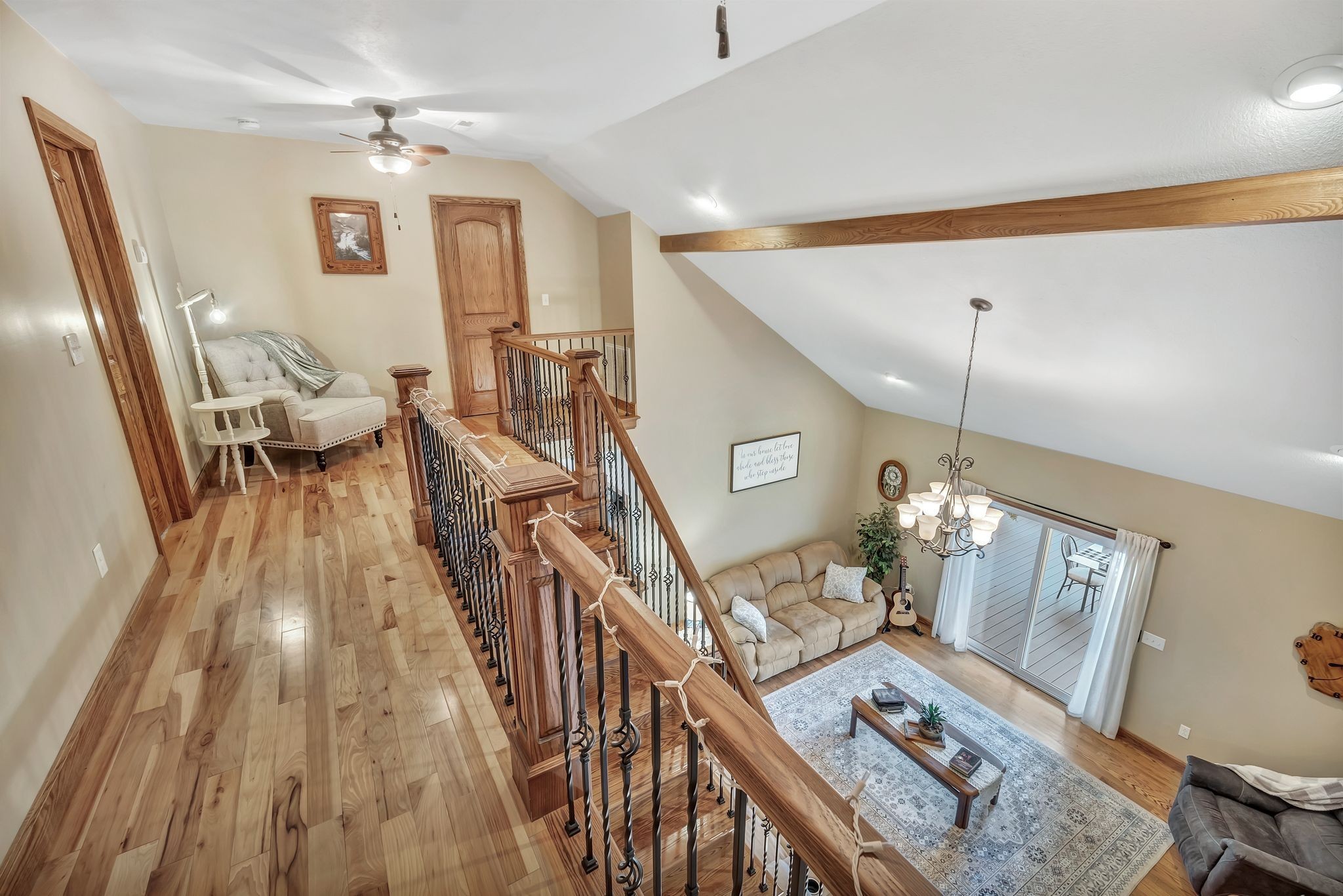 Open living room and upstairs landing with hardwood floors, wood-and-iron railing, vaulted ceiling, and chandelier.