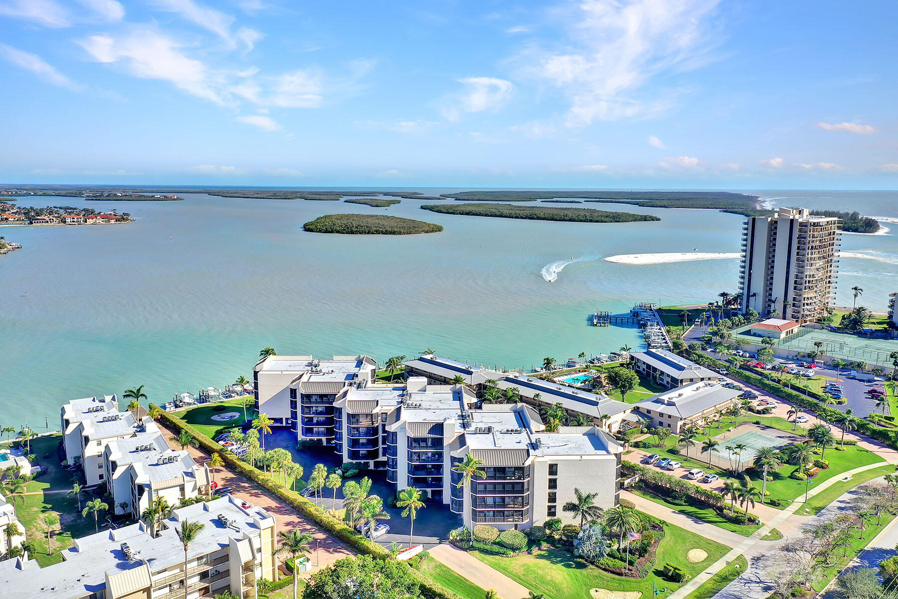 Waterfront condominiums beside a broad bay, with docks, mangrove islands, and the ocean beyond.