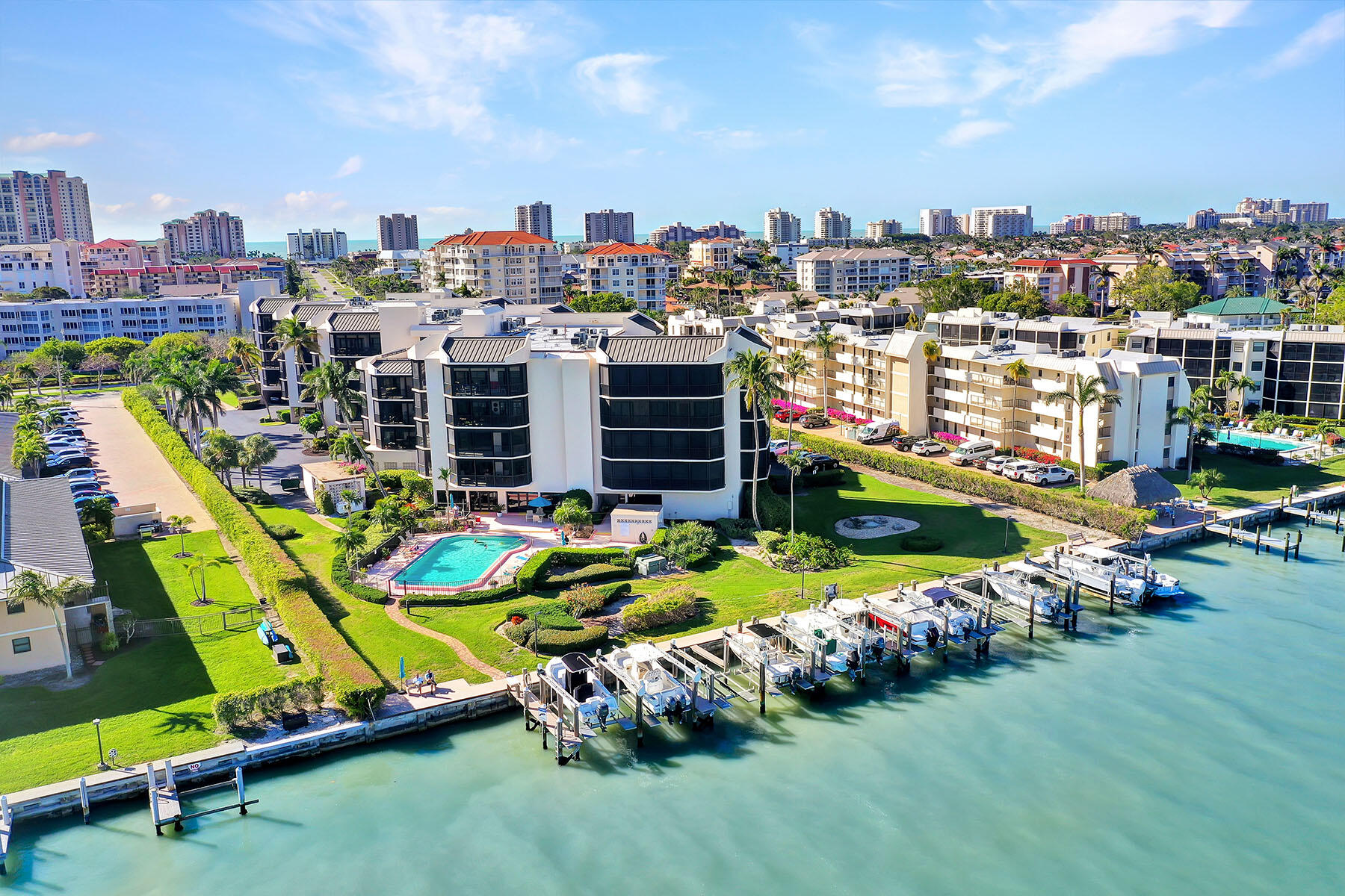 Aerial view of waterfront condominiums with a swimming pool, marina docks, and boats.