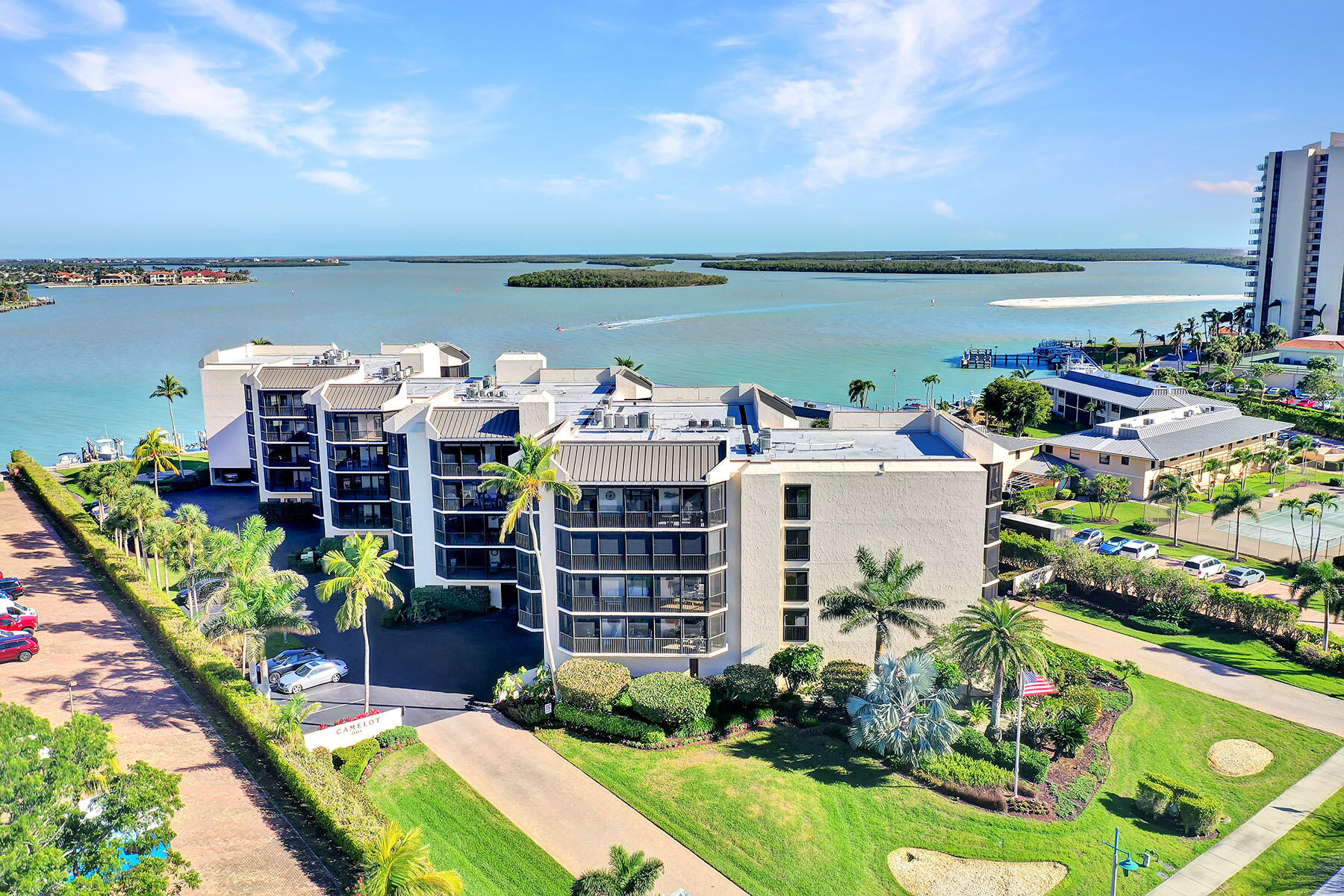 Aerial view of a waterfront condominium complex with landscaped grounds, docks, and island views.
