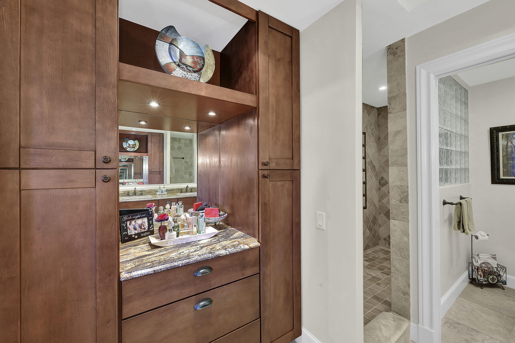 Bathroom vanity with rich wood cabinetry, a marbled counter, and a tiled shower beyond.
