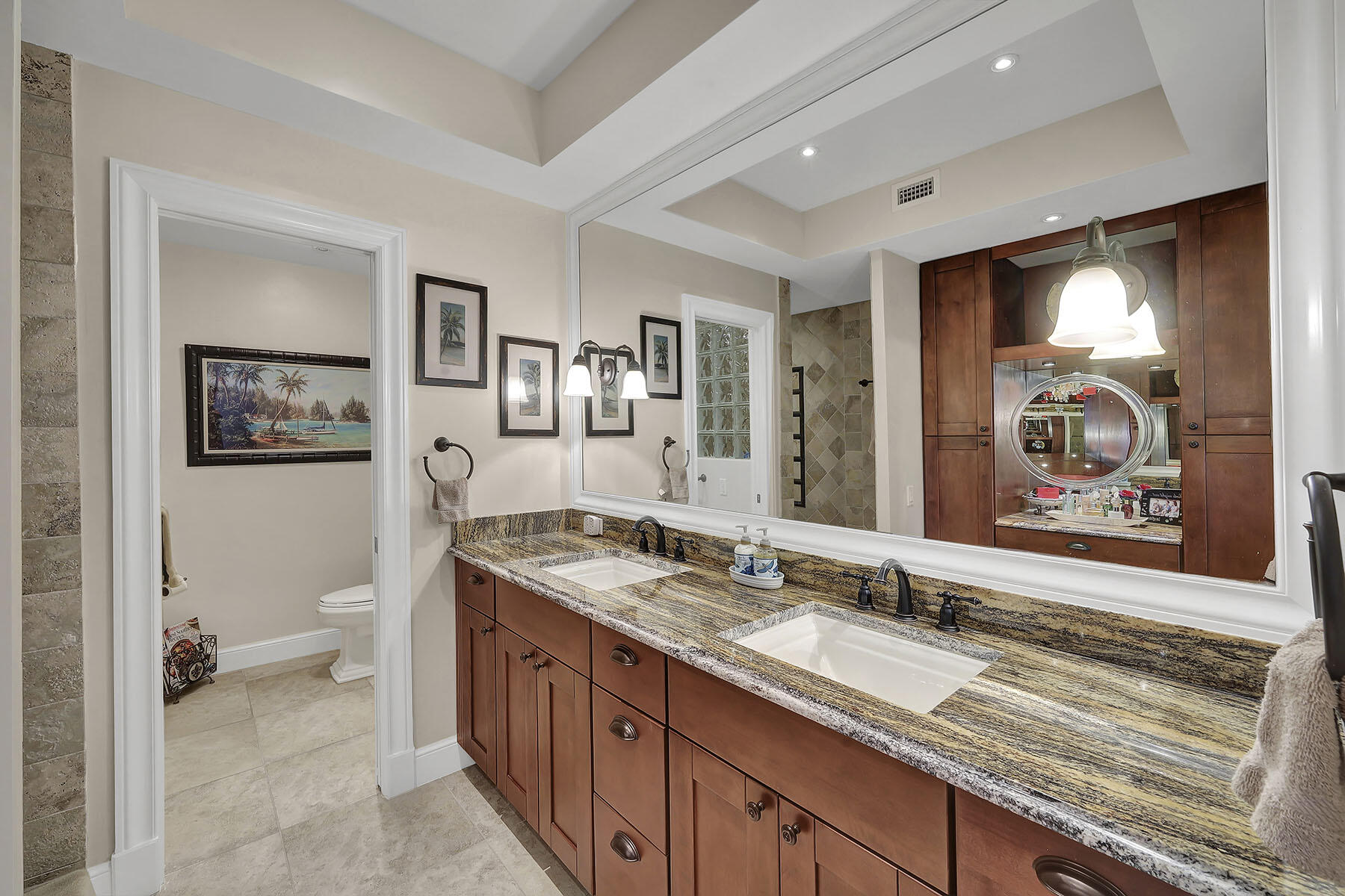 Bathroom with a granite double vanity, wood cabinetry, and a large mirror.