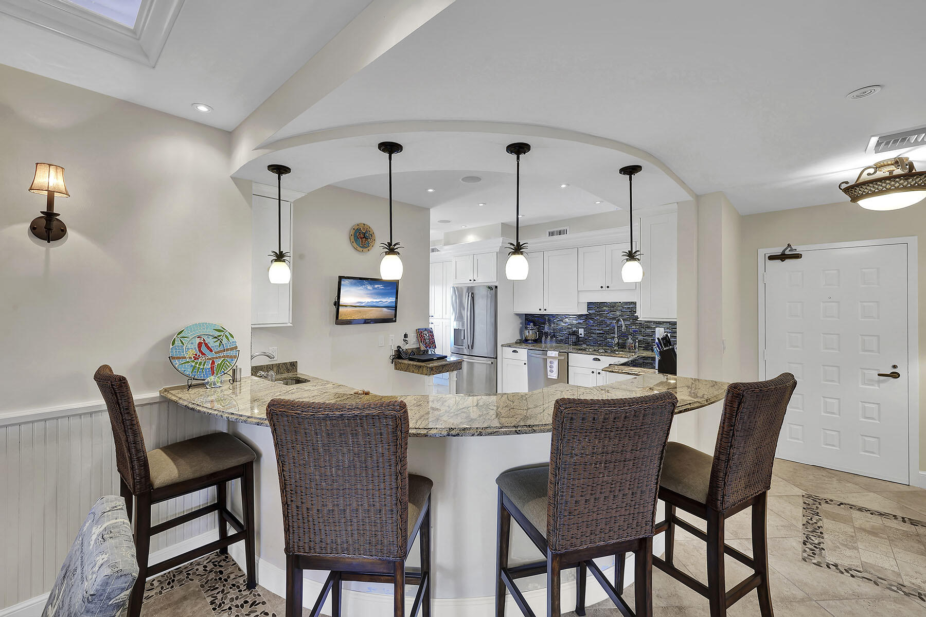 Kitchen with curved granite breakfast bar, woven stools, white cabinetry, and blue tile backsplash.
