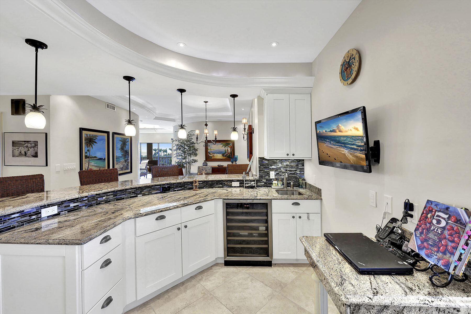 Open kitchen with curved granite breakfast bar, white cabinets, mosaic backsplash, and built-in wine refrigerator.