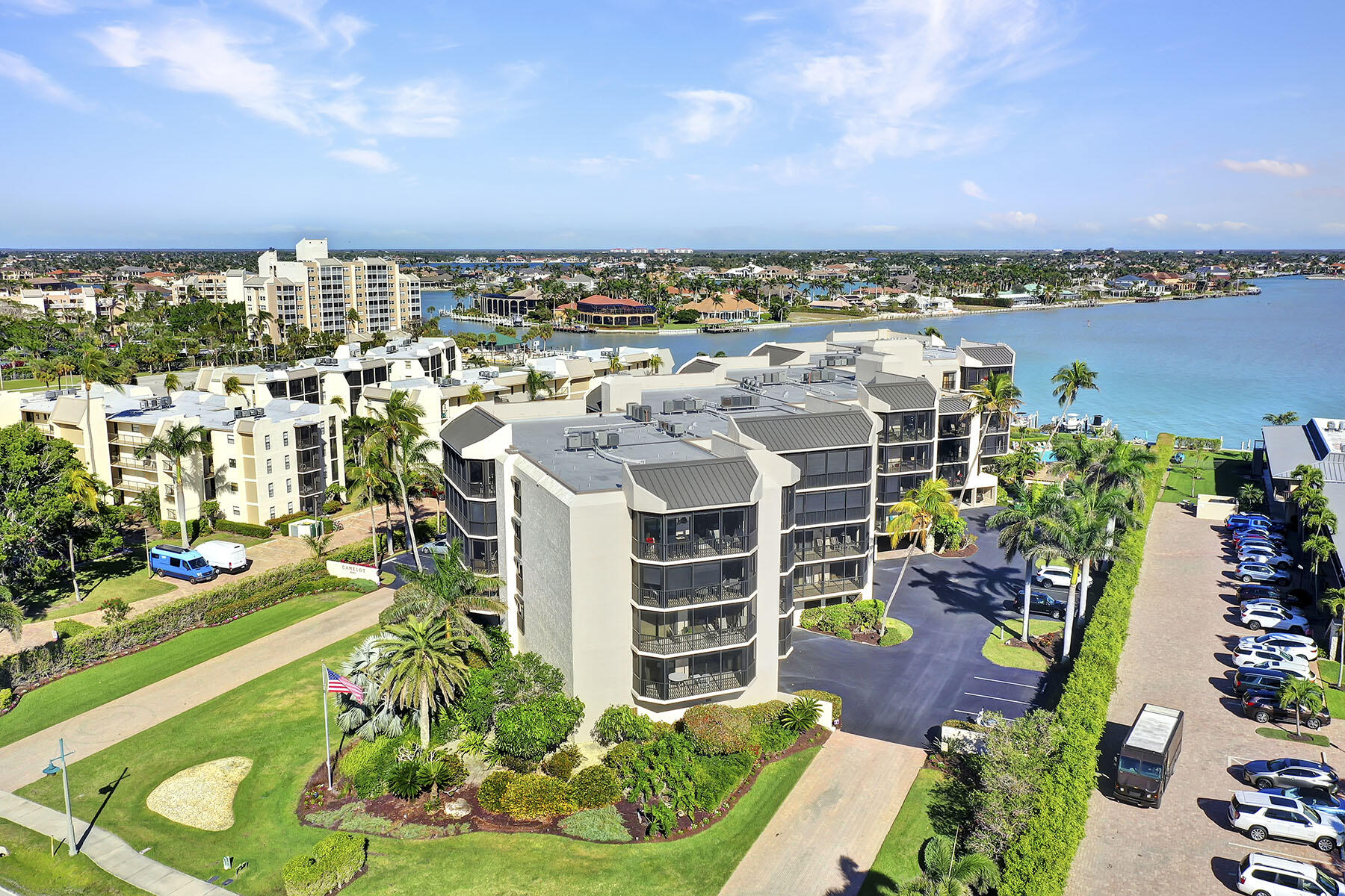 Waterfront condominium complex surrounded by palm trees, with a broad waterway and neighborhood in the distance.