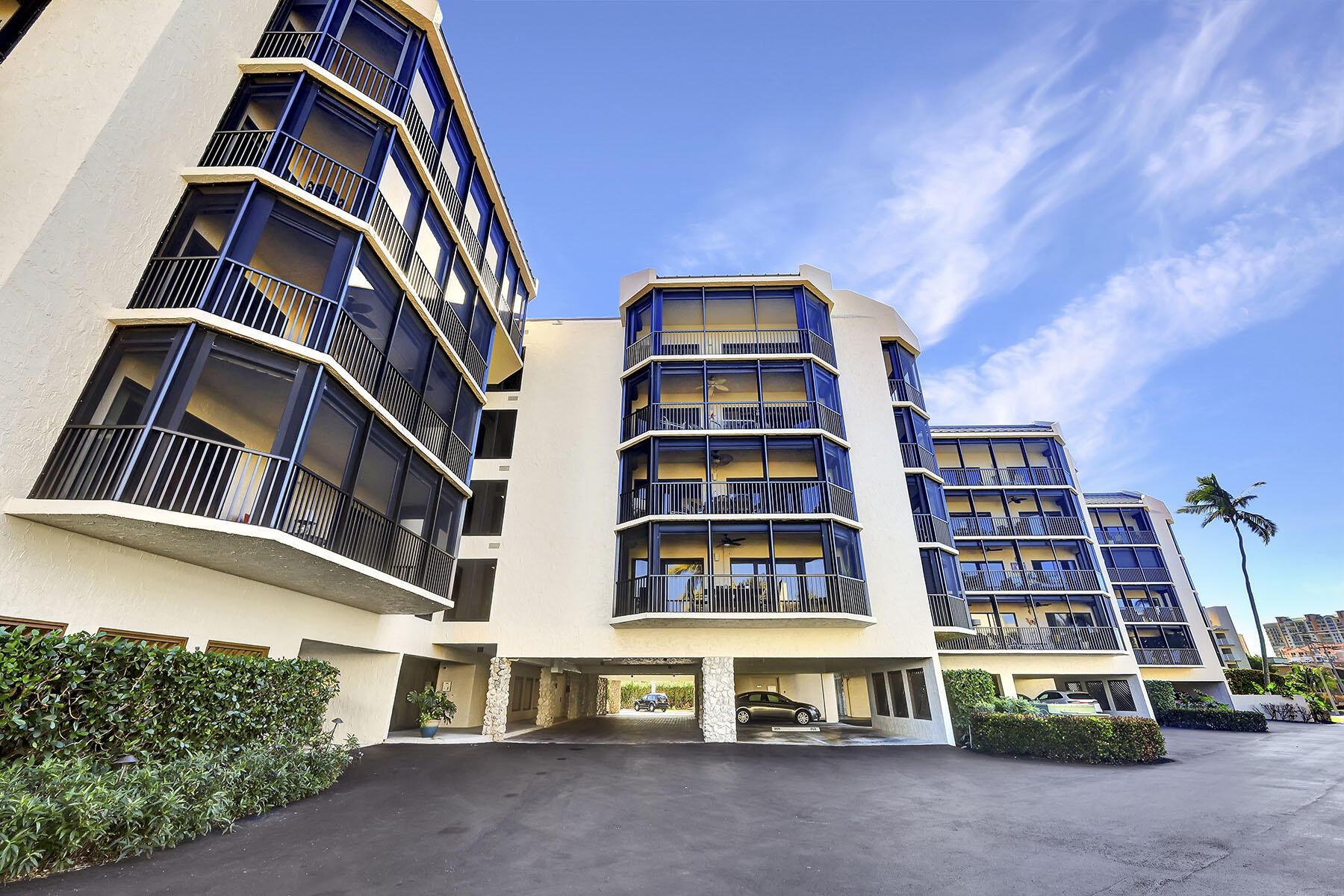 Condominium building with blue-framed balconies and covered parking beneath a bright blue sky.