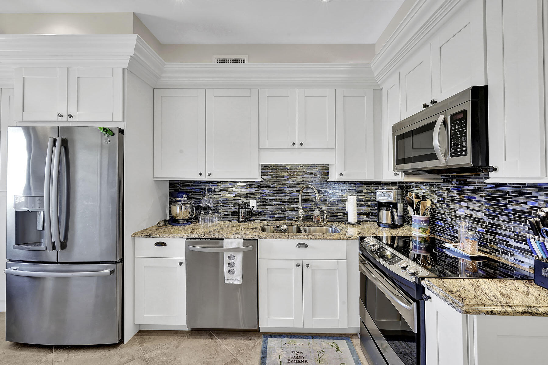 Kitchen with white cabinets, stainless steel appliances, granite counters, and a blue-gray mosaic backsplash.
