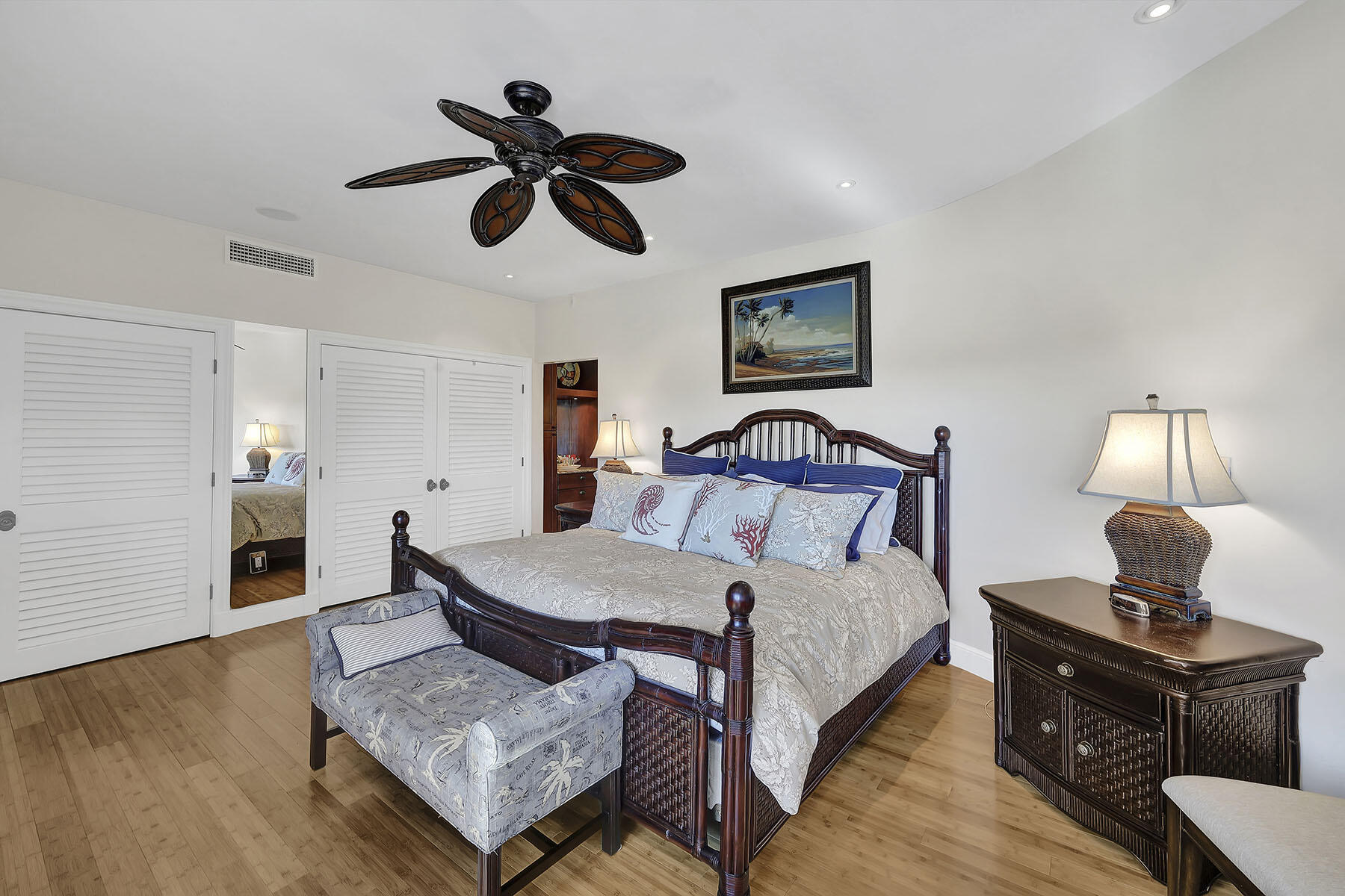 Furnished bedroom with a dark wood bed, patterned bedding, upholstered bench, and hardwood floors.