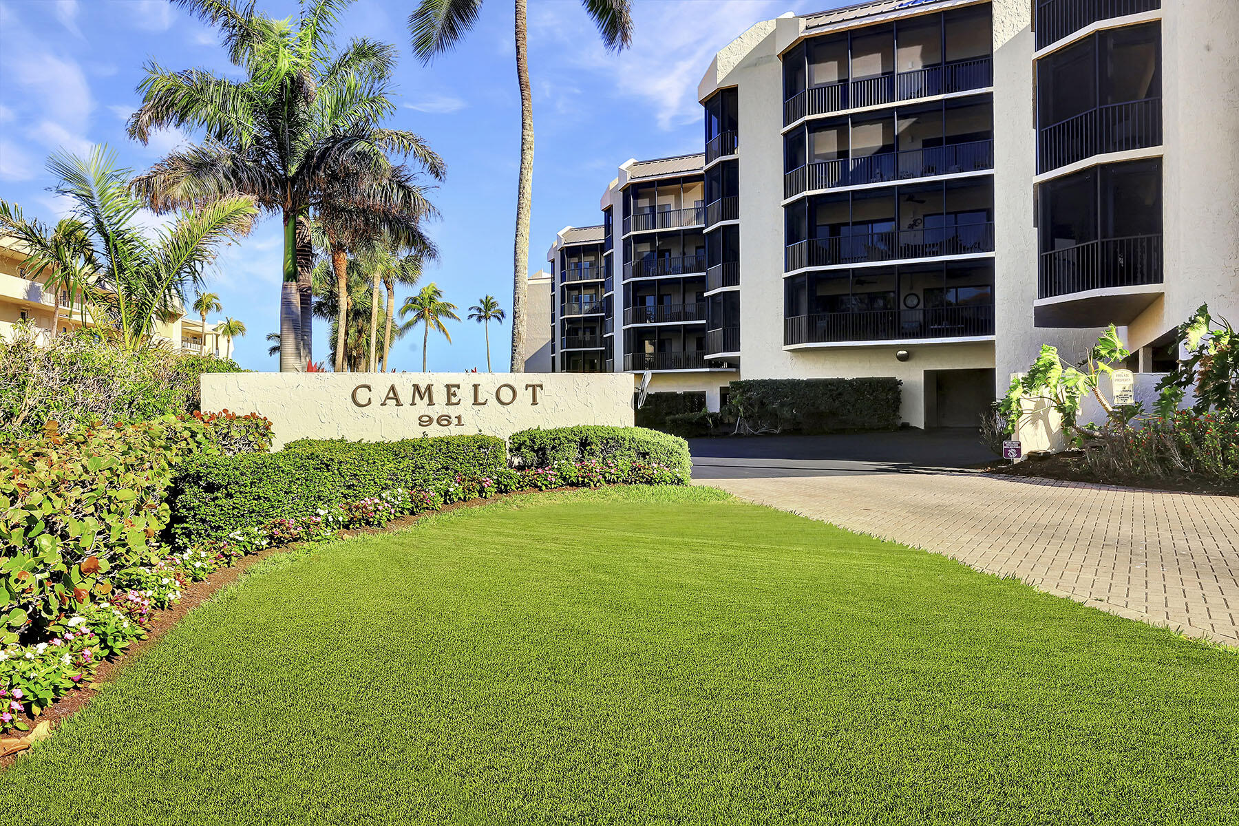 Camelot 961 condominium exterior with palm trees, landscaped grounds, and screened balconies.