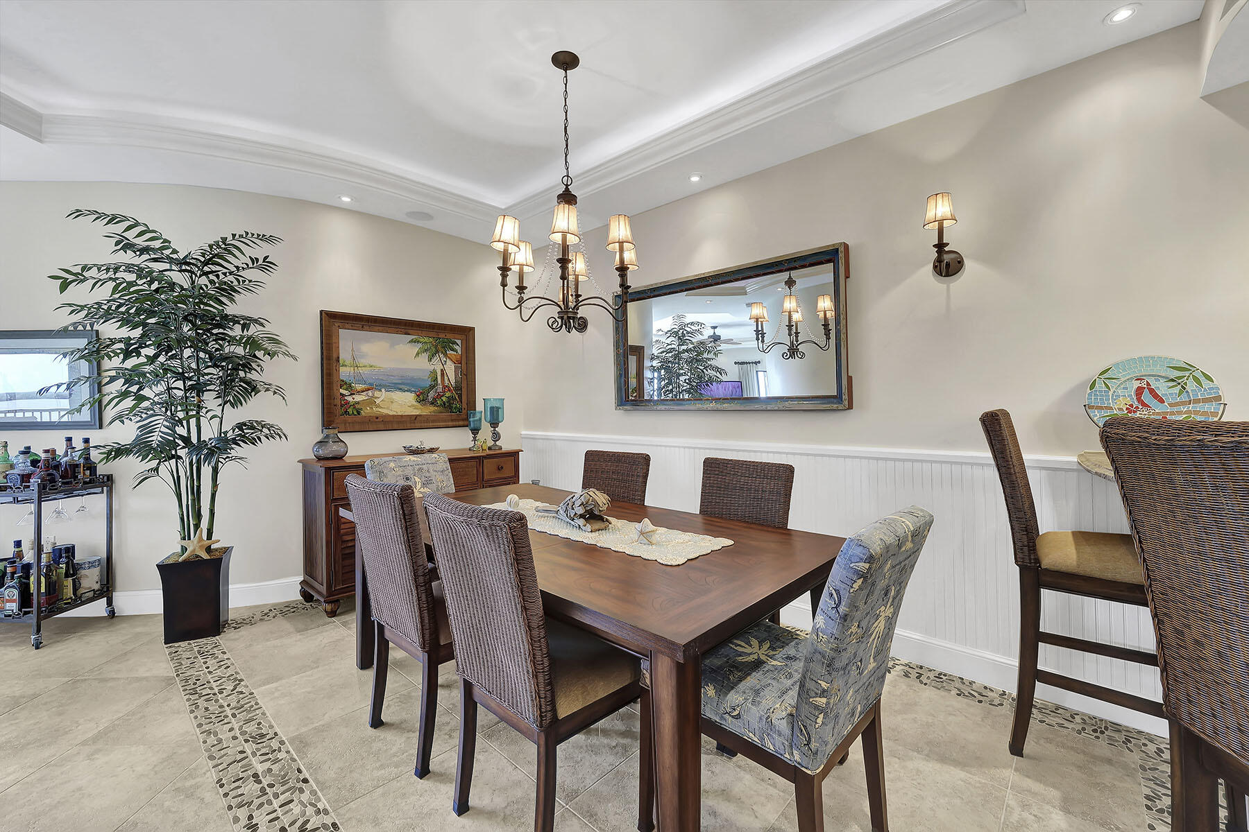 Dining room with a dark wood table, woven chairs, chandelier, and large wall mirror.
