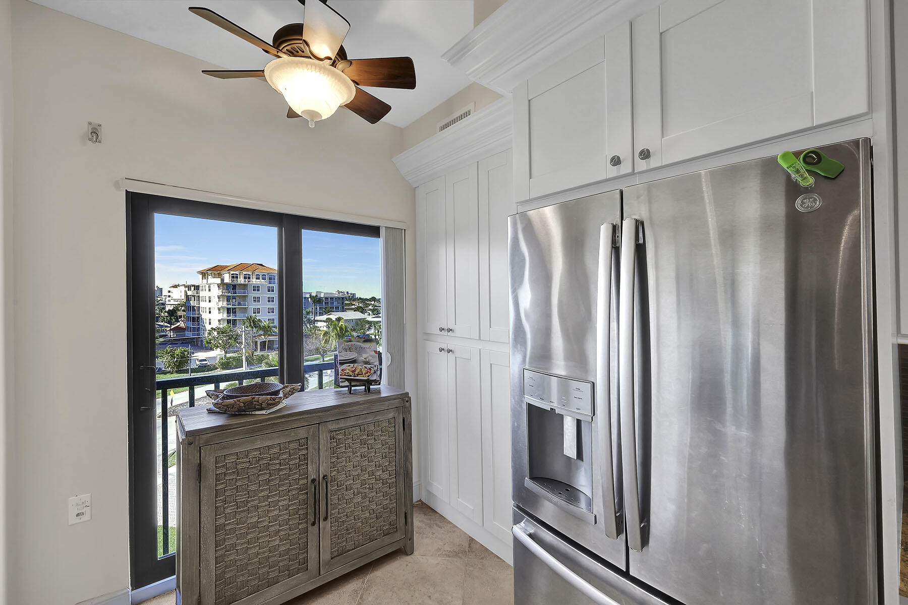 Kitchen with white cabinetry and stainless refrigerator beside a glass door overlooking nearby buildings.