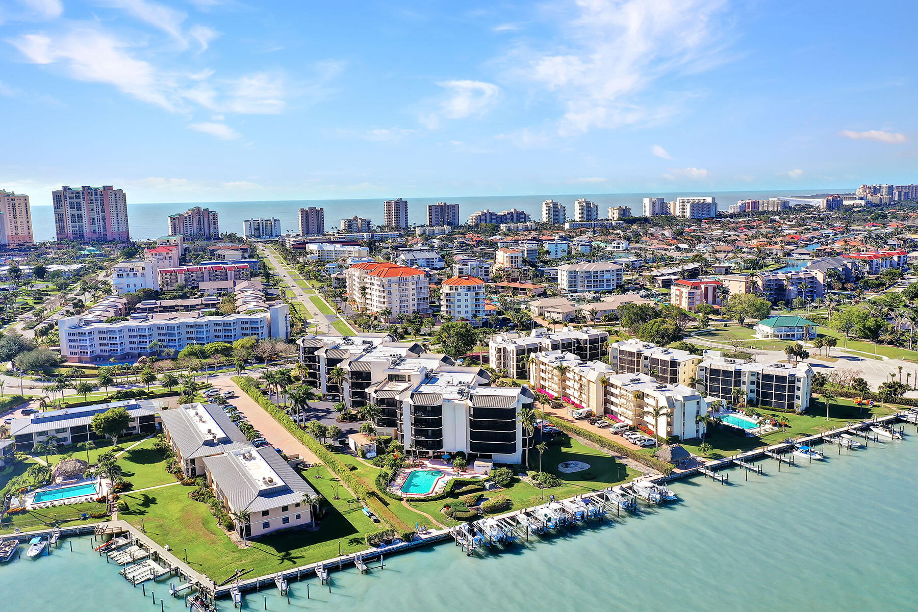 Aerial view of waterfront condominiums, boat docks, and pools beside the sea.