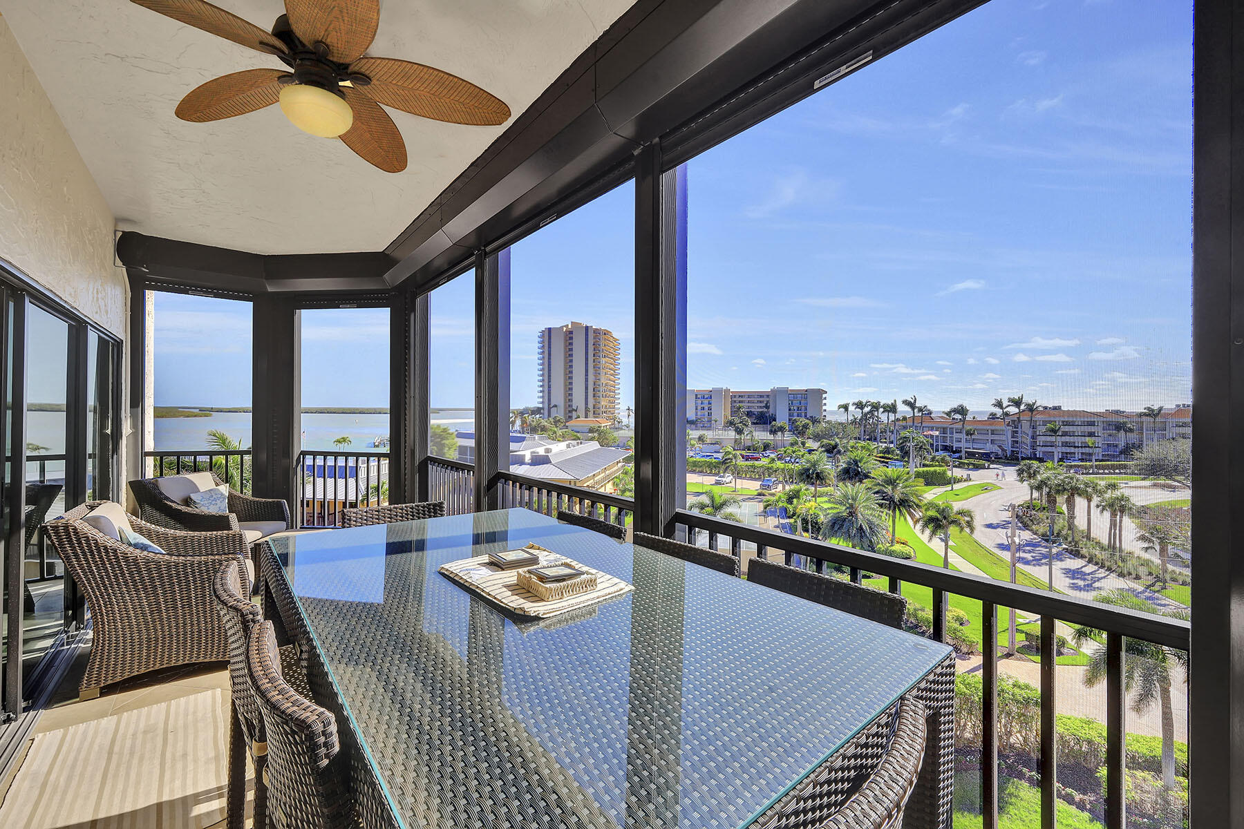 Screened balcony with wicker dining set overlooking landscaped grounds and water.