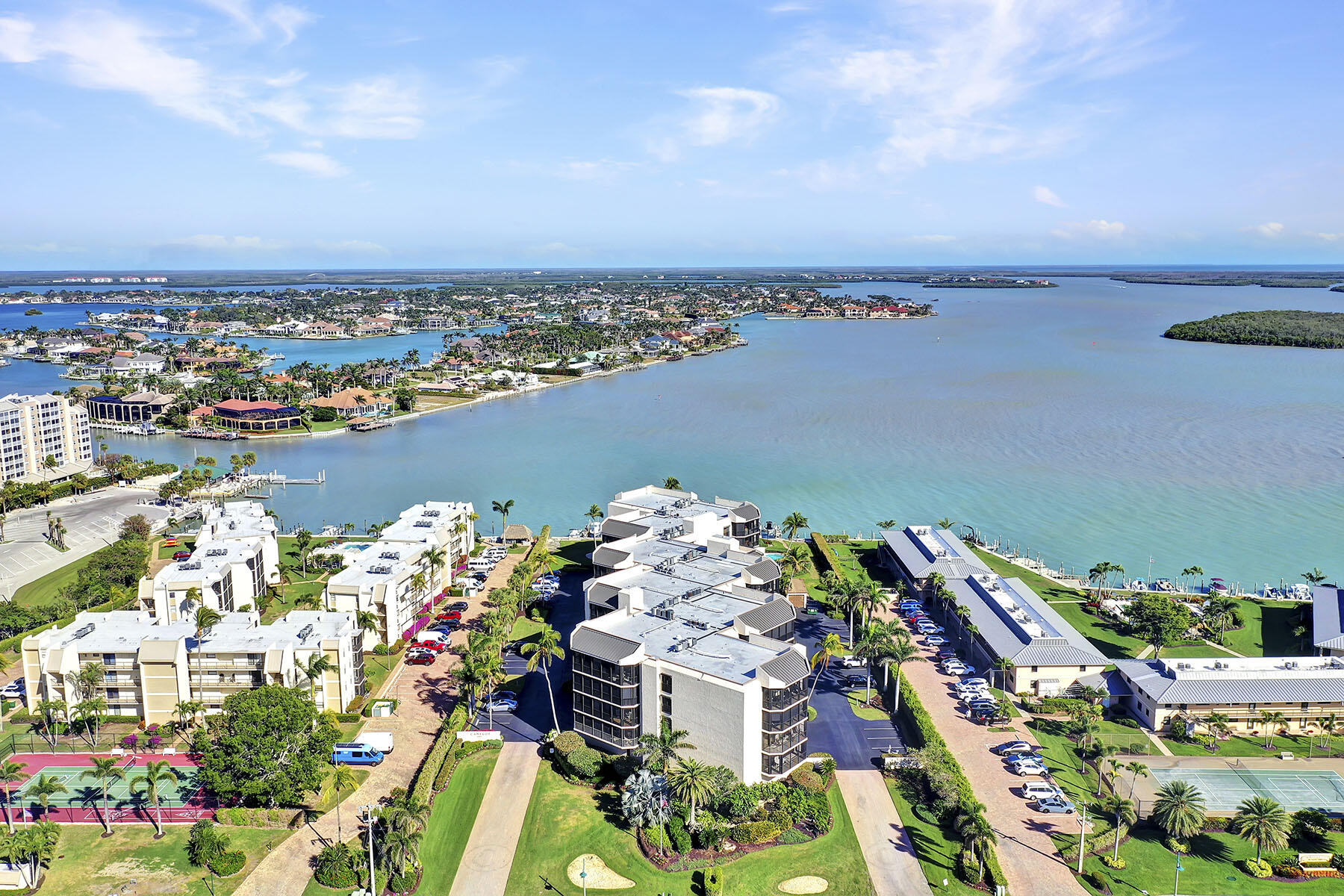Waterfront condominiums overlooking a broad bay, with landscaped grounds and tennis courts.