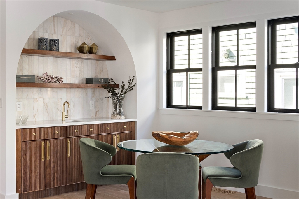 Dining nook with a round glass table, green chairs, and a marble-backed built-in bar.